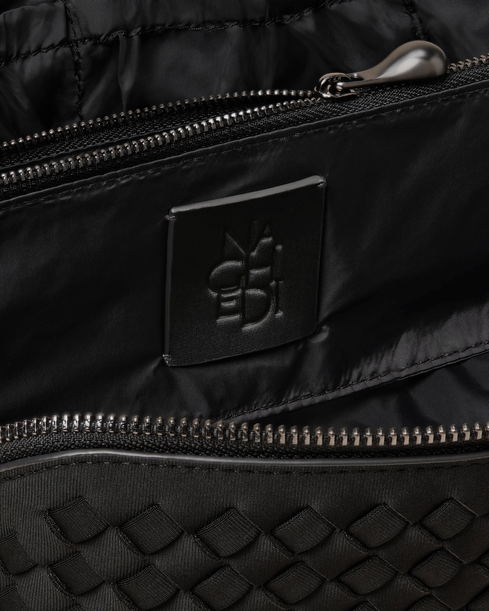Close-up of stamped NAGHEDI logo, interior pocket and wipe-clean nylon lining in Caravan Cosmetic Case in Onyx.