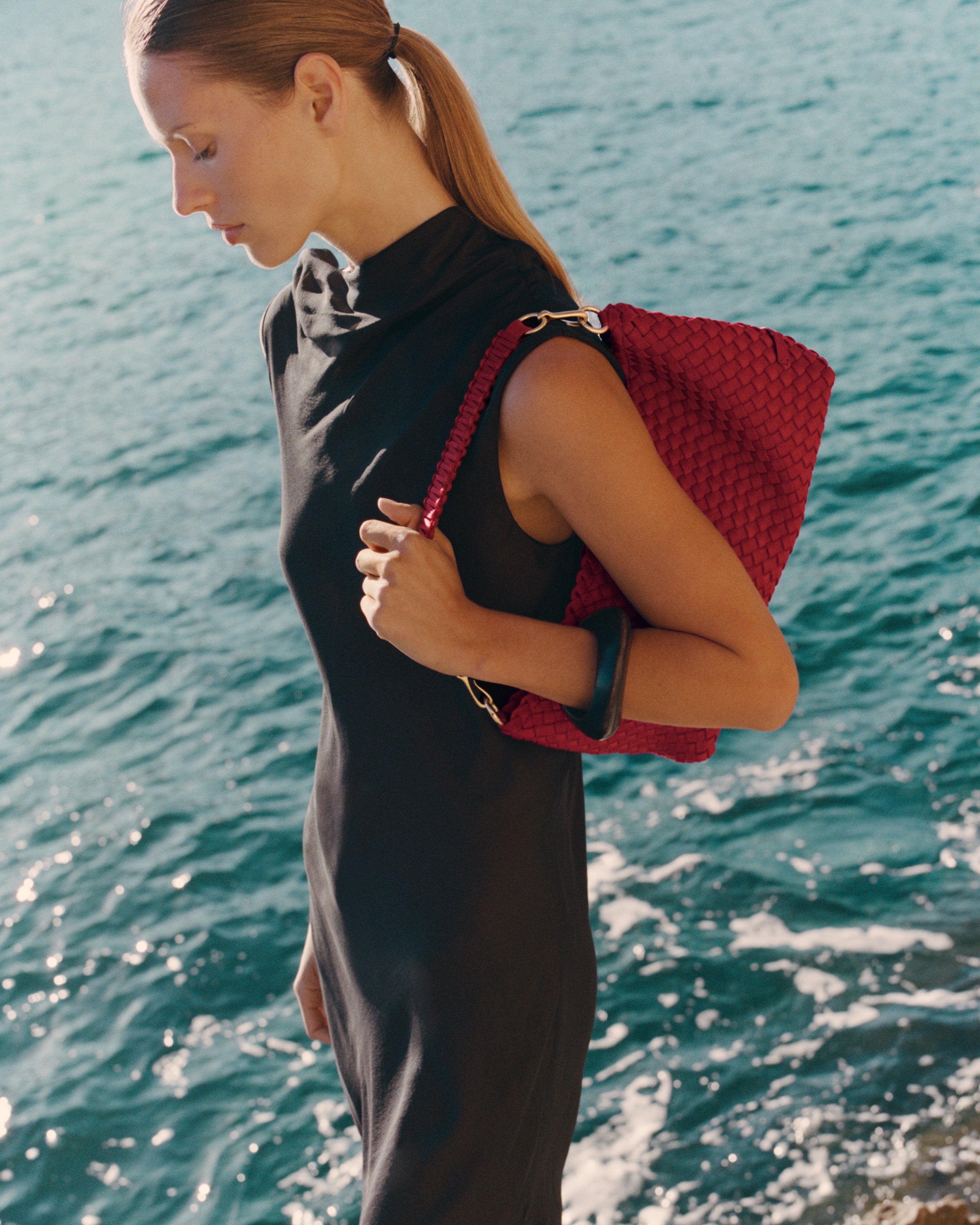 On model close-up of Porto Half-Moon in Rosso showing its hand stitched strap and handwoven neoprene design.