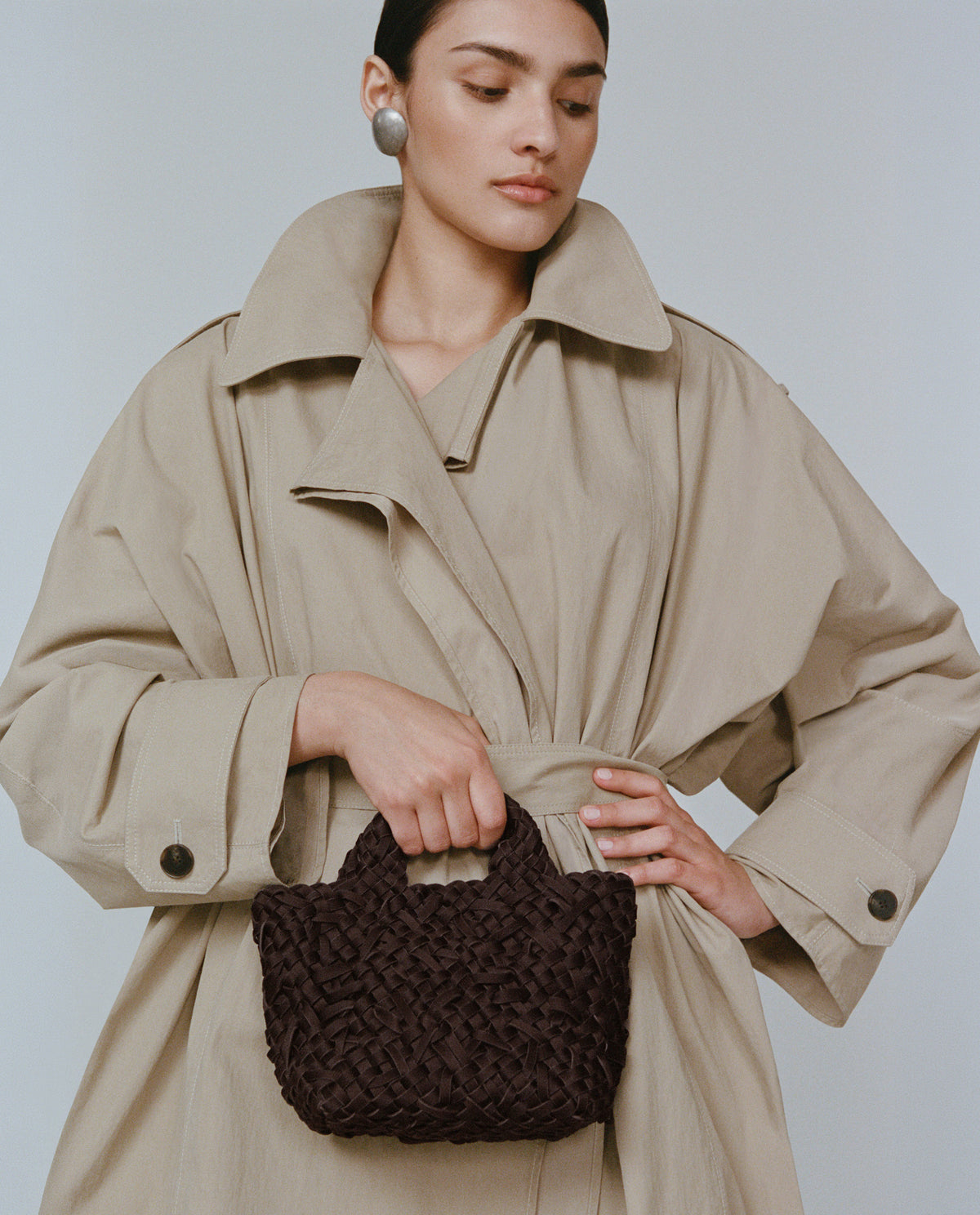 A model holding the St. Barths Petit Tote in a chocolate brown handwoven nest weave pattern.