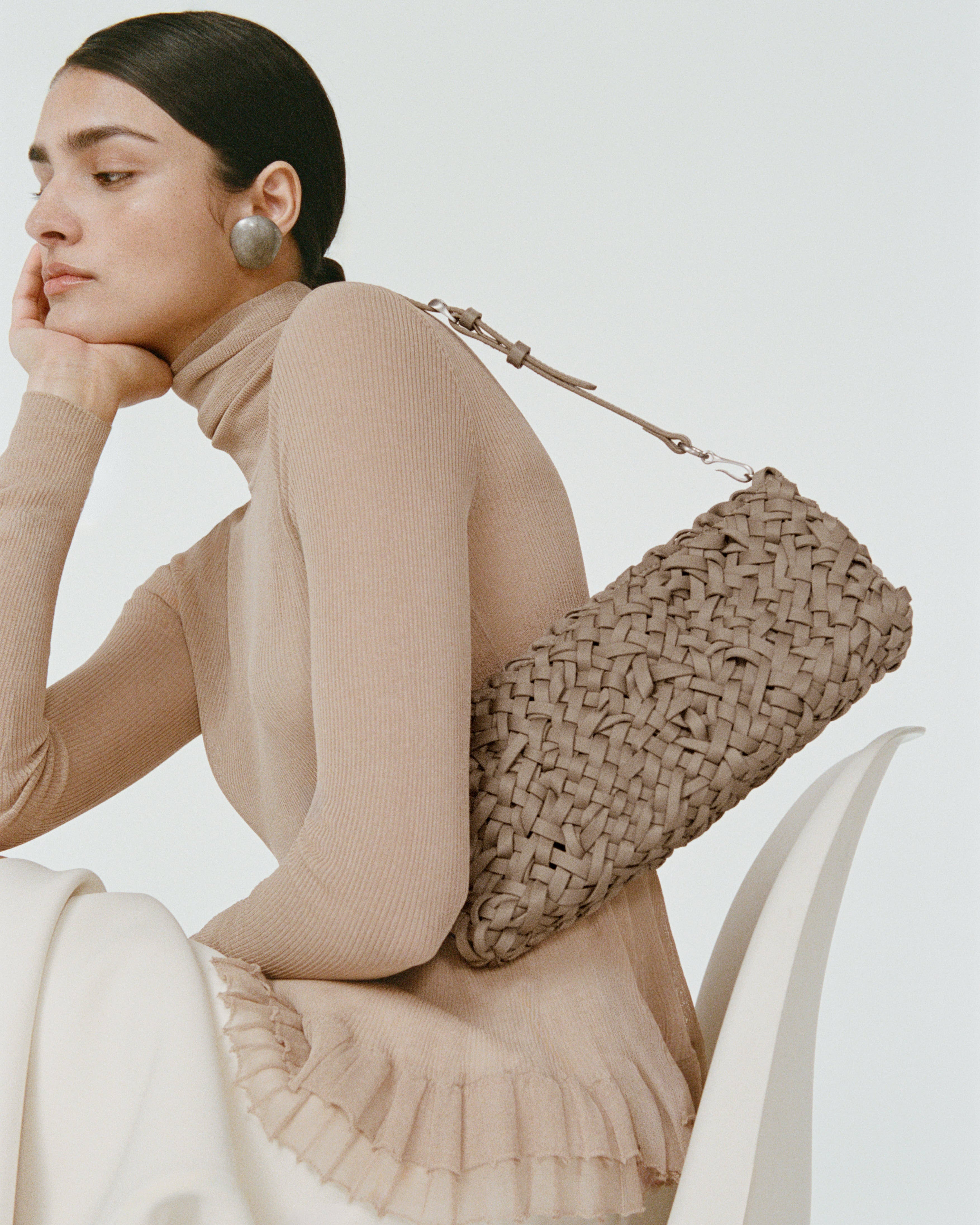 Model wearing handwoven neoprene shoulder bag in cool taupe color with a crosshatch nest weave pattern and silver hardware over her shoulder.