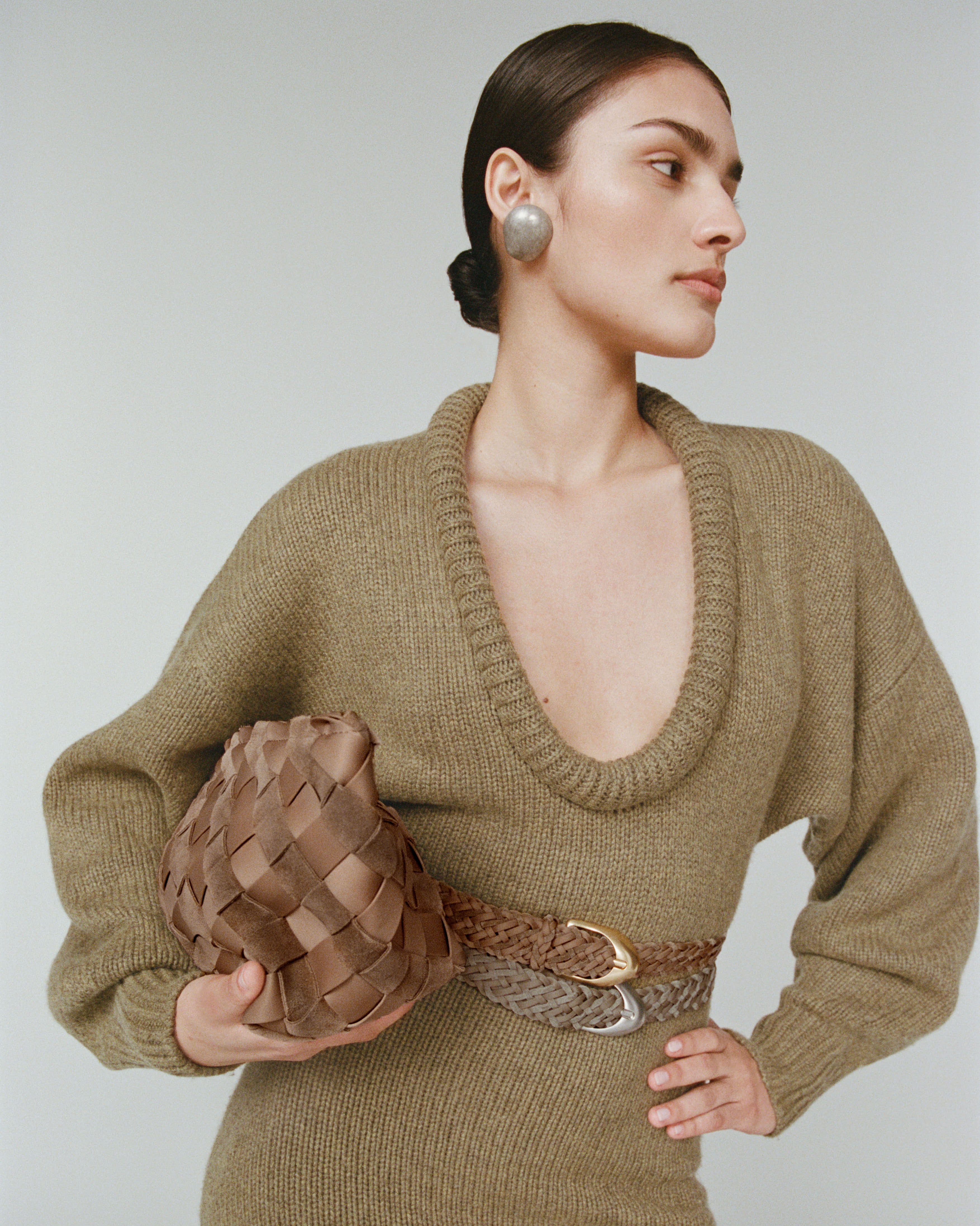 Model wearing a green dress holding the Gigi Clutch in a light brown handwoven suede and neoprene material