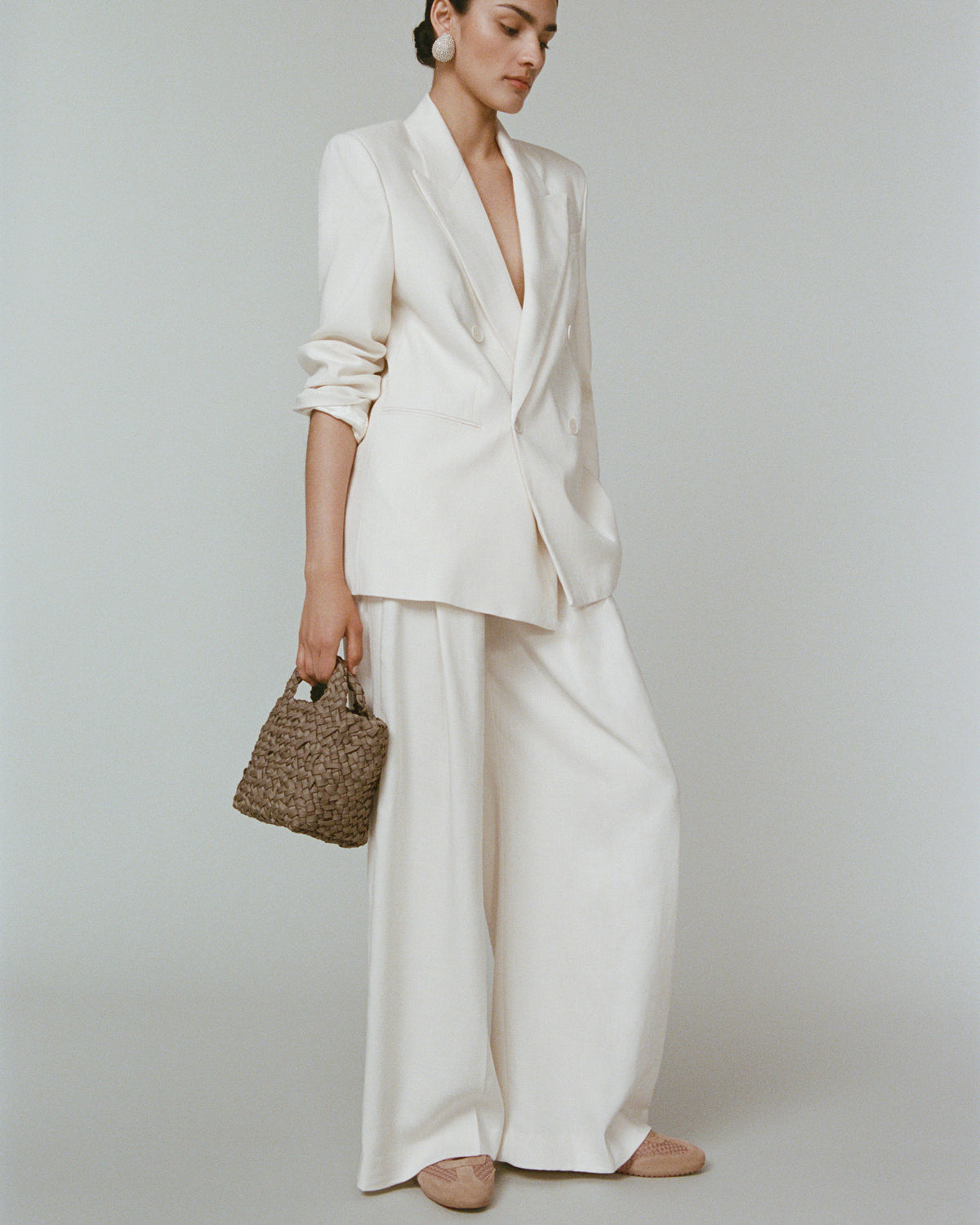 Model wearing a cool taupe woven basket-style neoprene handbag with a top handle 