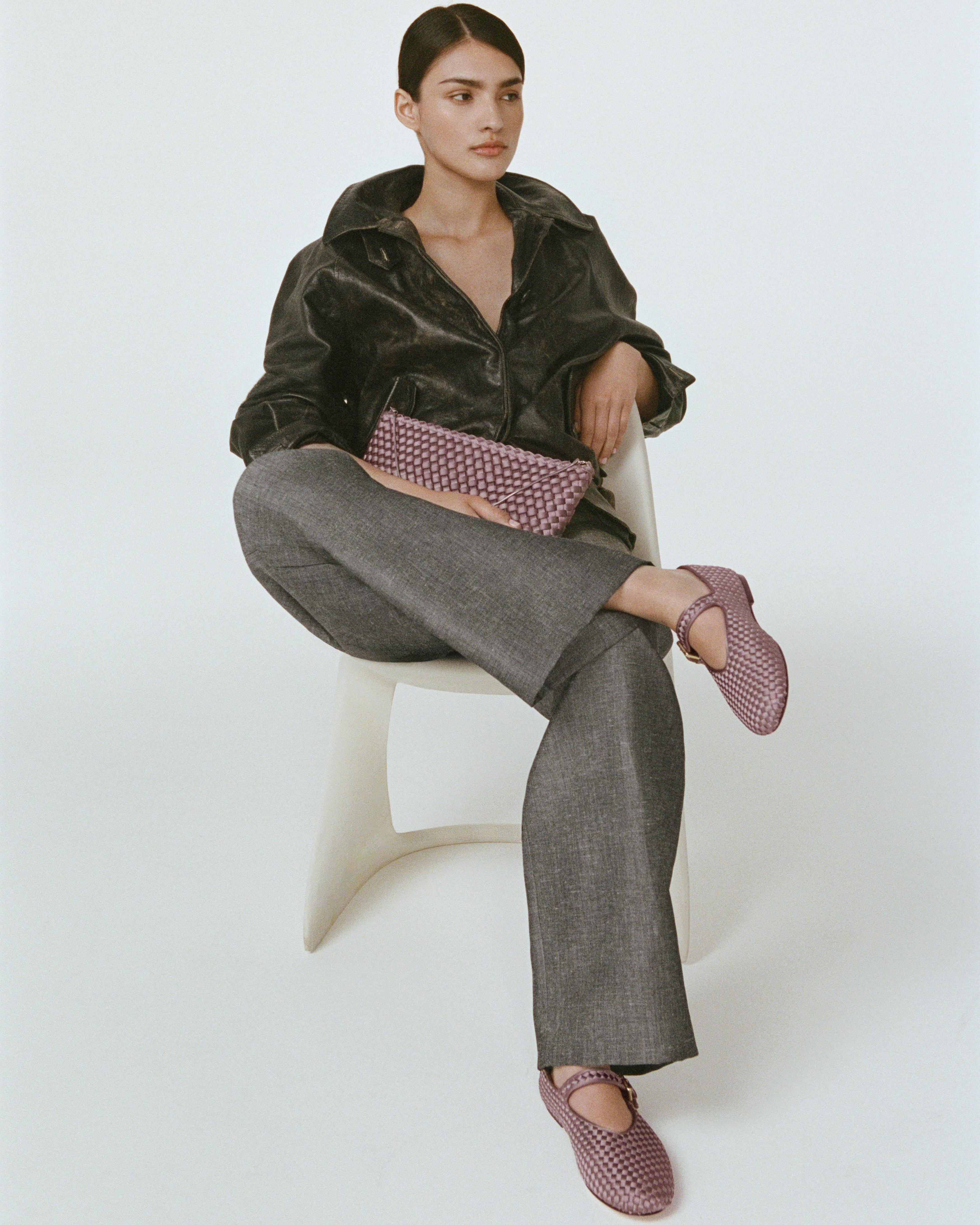 Model wearing a pair of the Marais Mary Jane in Lavender sitting with her legs crossed and holding a matching Gala Clutch.