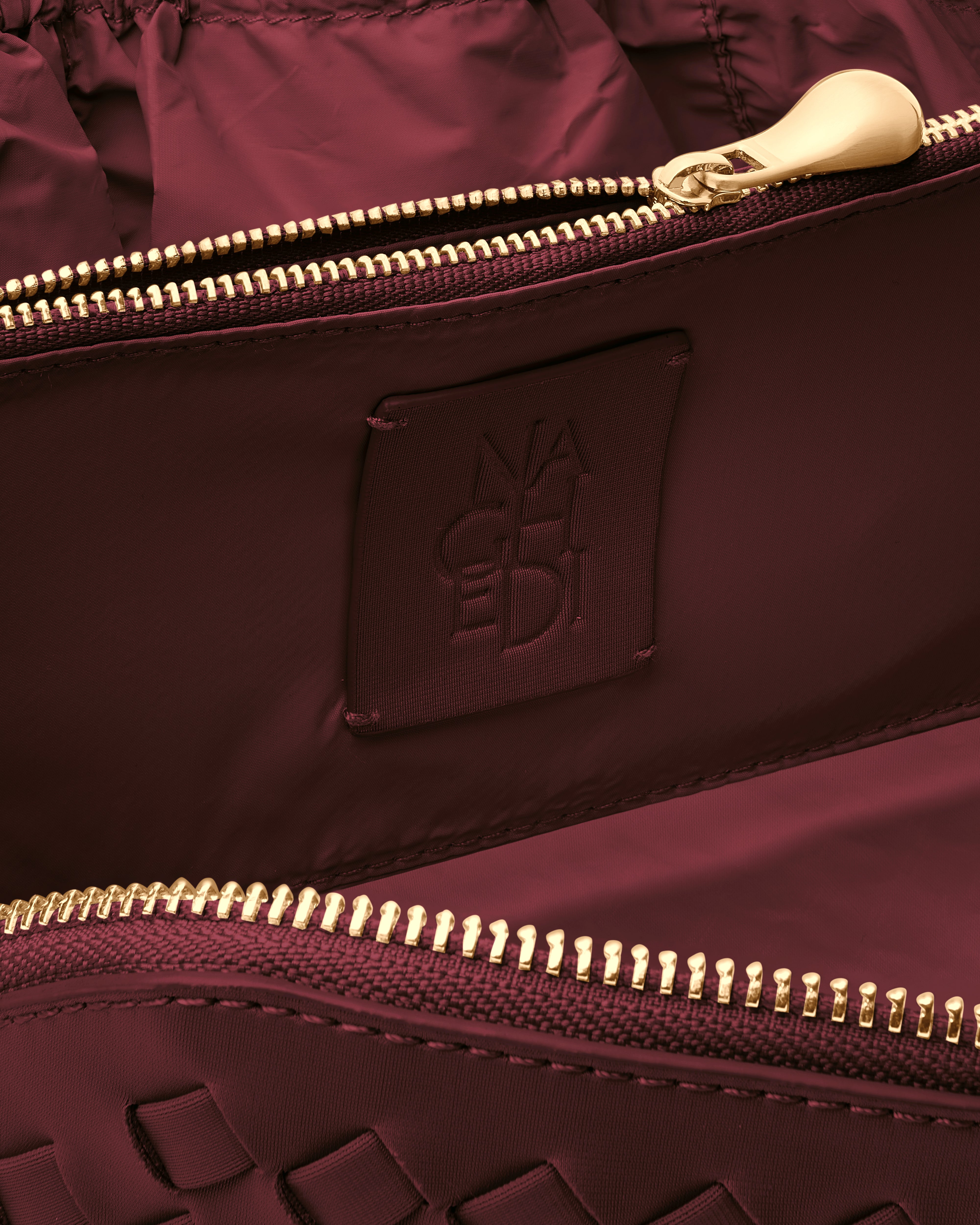 Close-up of stamped NAGHEDI logo, interior pocket and wipe-clean nylon lining in Caravan Cosmetic Case in Bordeaux.
