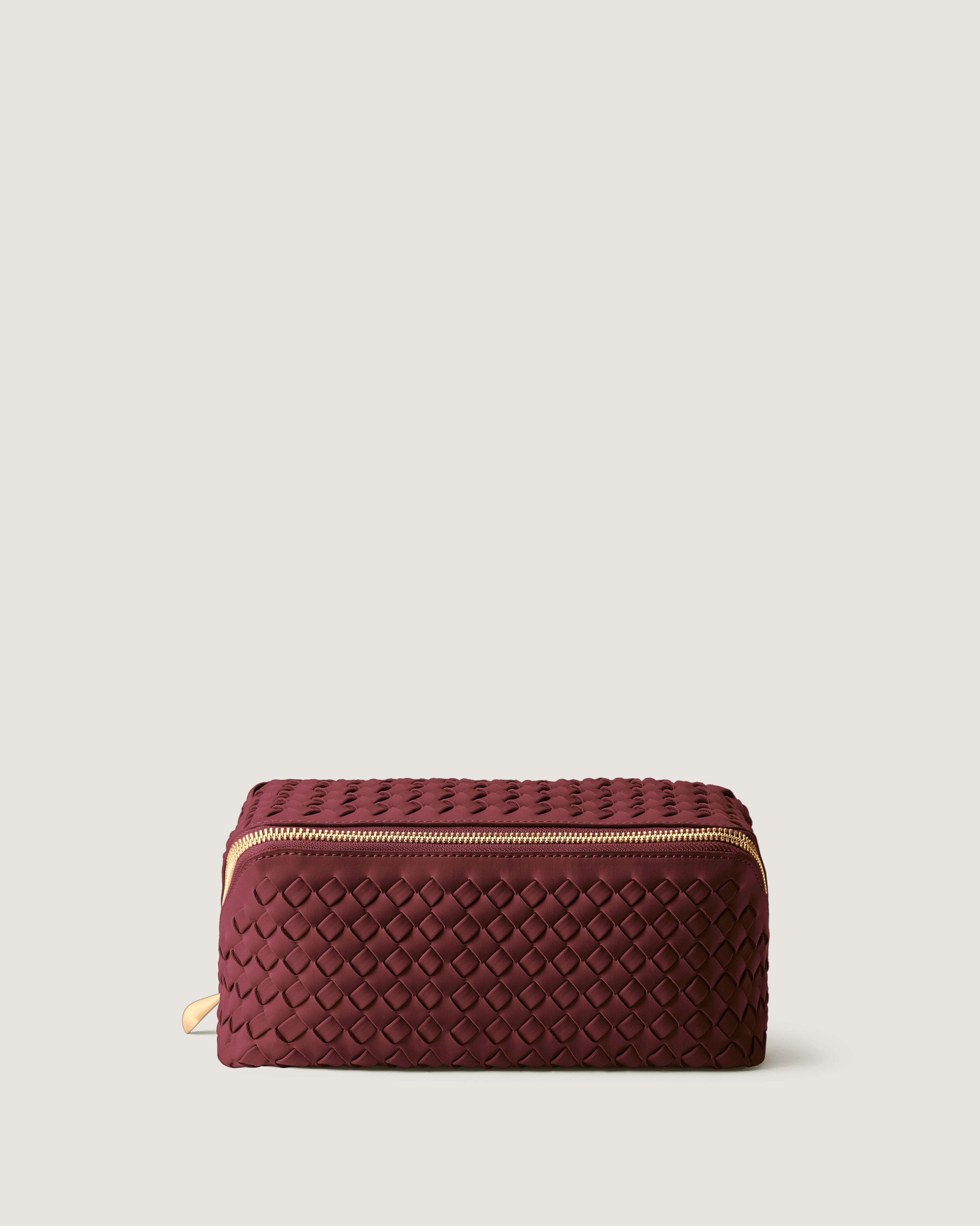Caravan Cosmetic Case in Bordeaux, a burgundy tone, in handwoven neoprene, featuring a wrap-around zip closure.