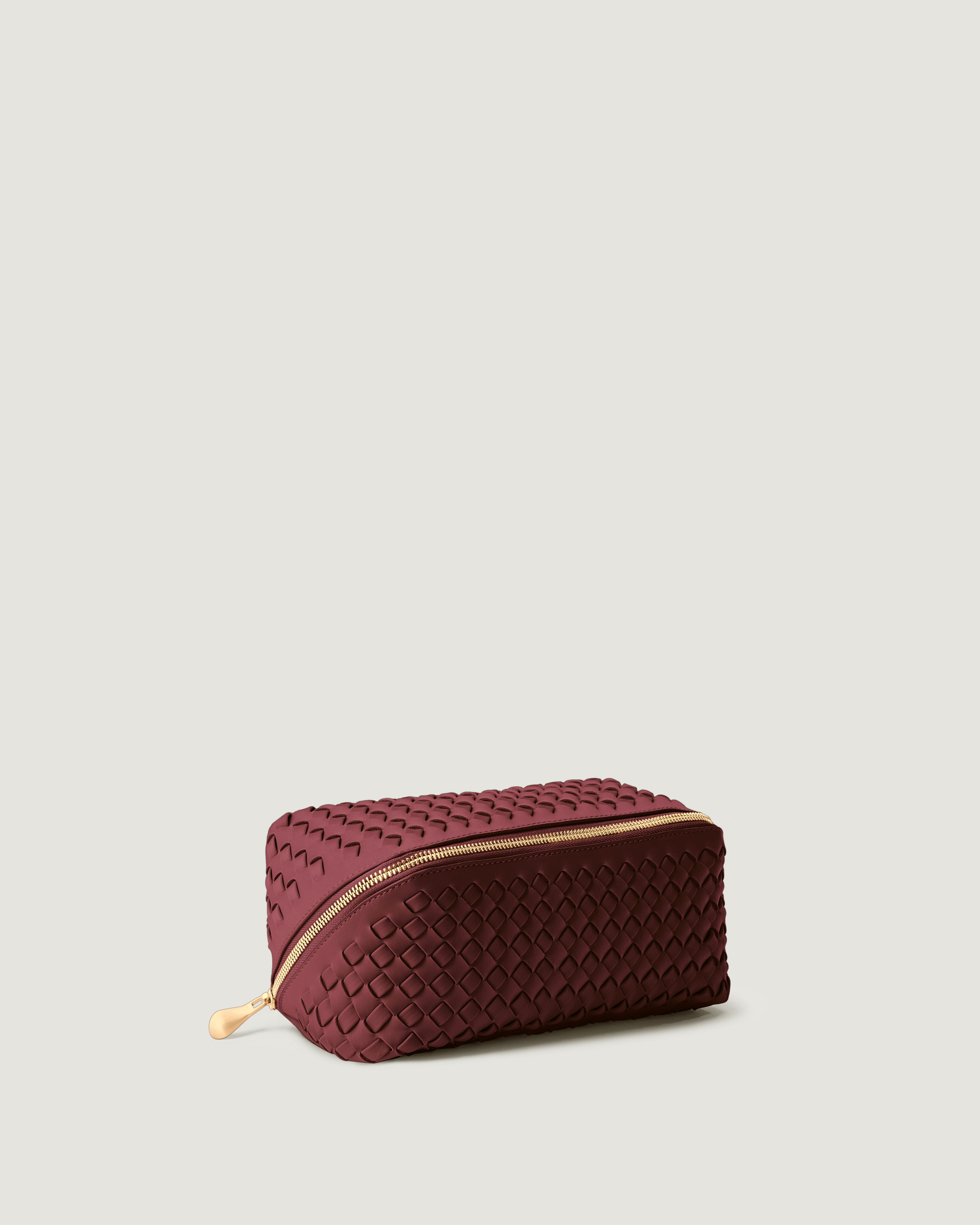 Caravan Cosmetic Case in Bordeaux shown from a side angle, highlighting its handwoven neoprene construction and wrap-around zip closure.