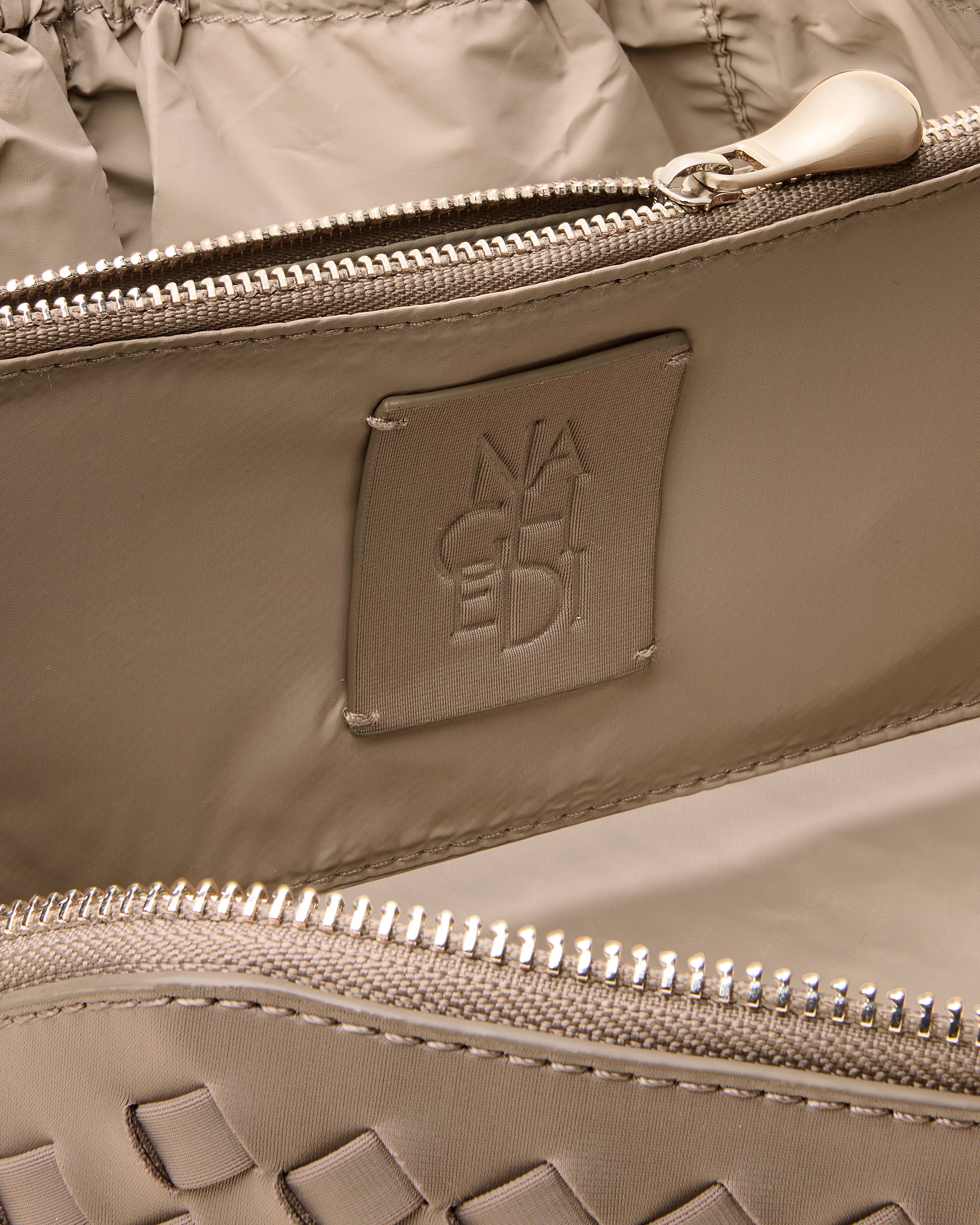 Close-up of stamped NAGHEDI logo, interior pocket and wipe-clean nylon lining in Caravan Cosmetic Case in Cashmere.