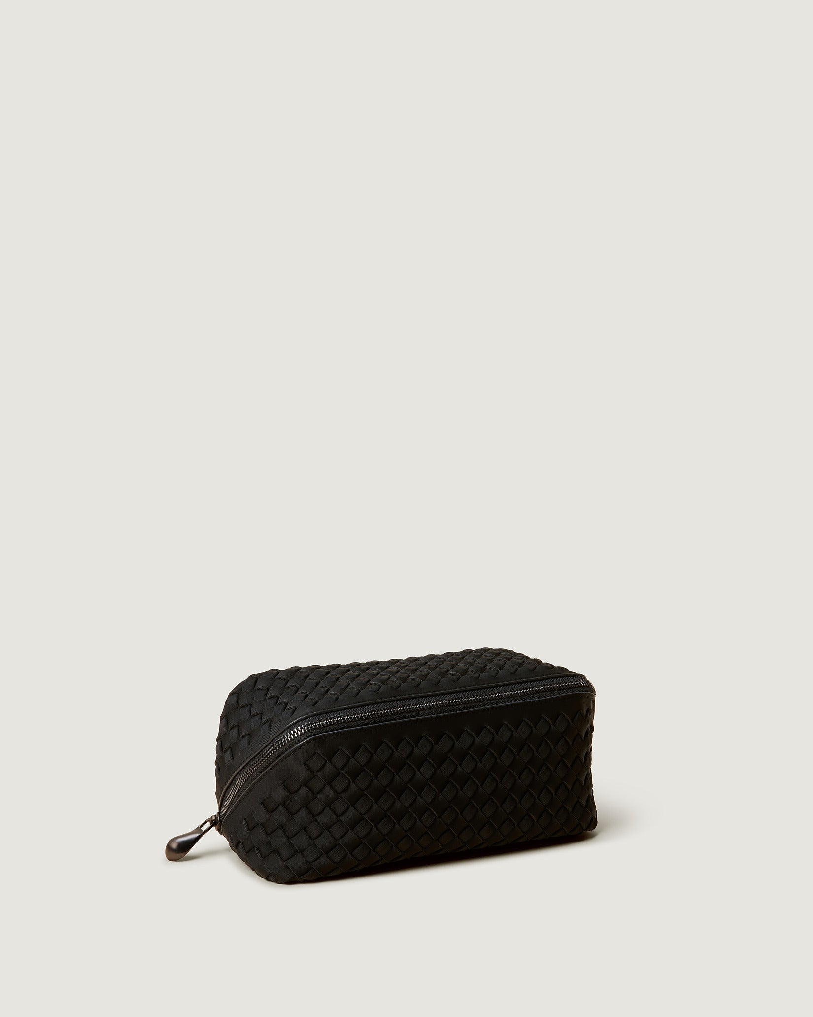 Caravan Medium Cosmetic Case in Onyx shown from a side angle, highlighting its handwoven neoprene and wrap-around zip closure.