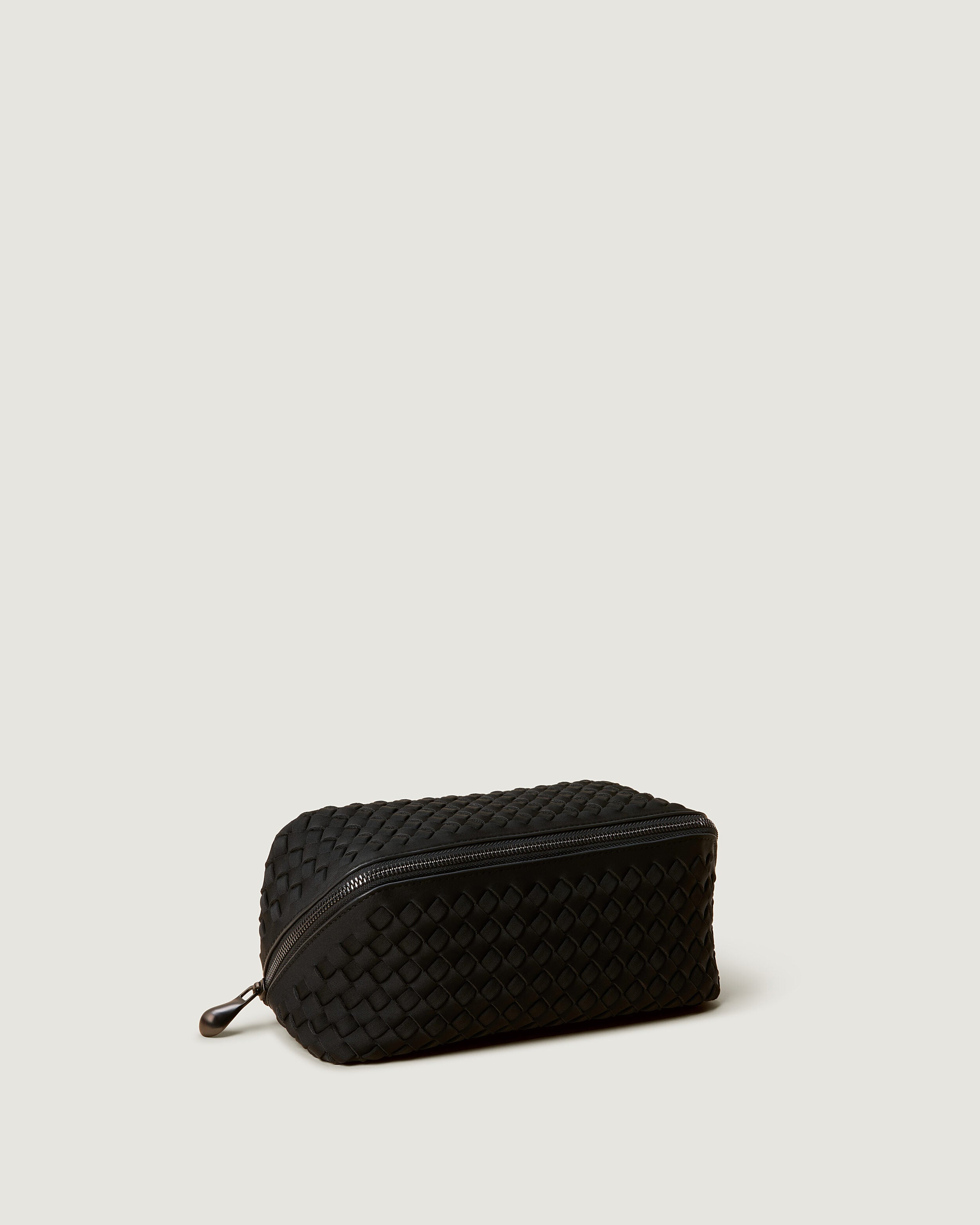 Caravan Cosmetic Case in Onyx shown from a side angle, highlighting its handwoven neoprene construction and wrap-around zip closure.