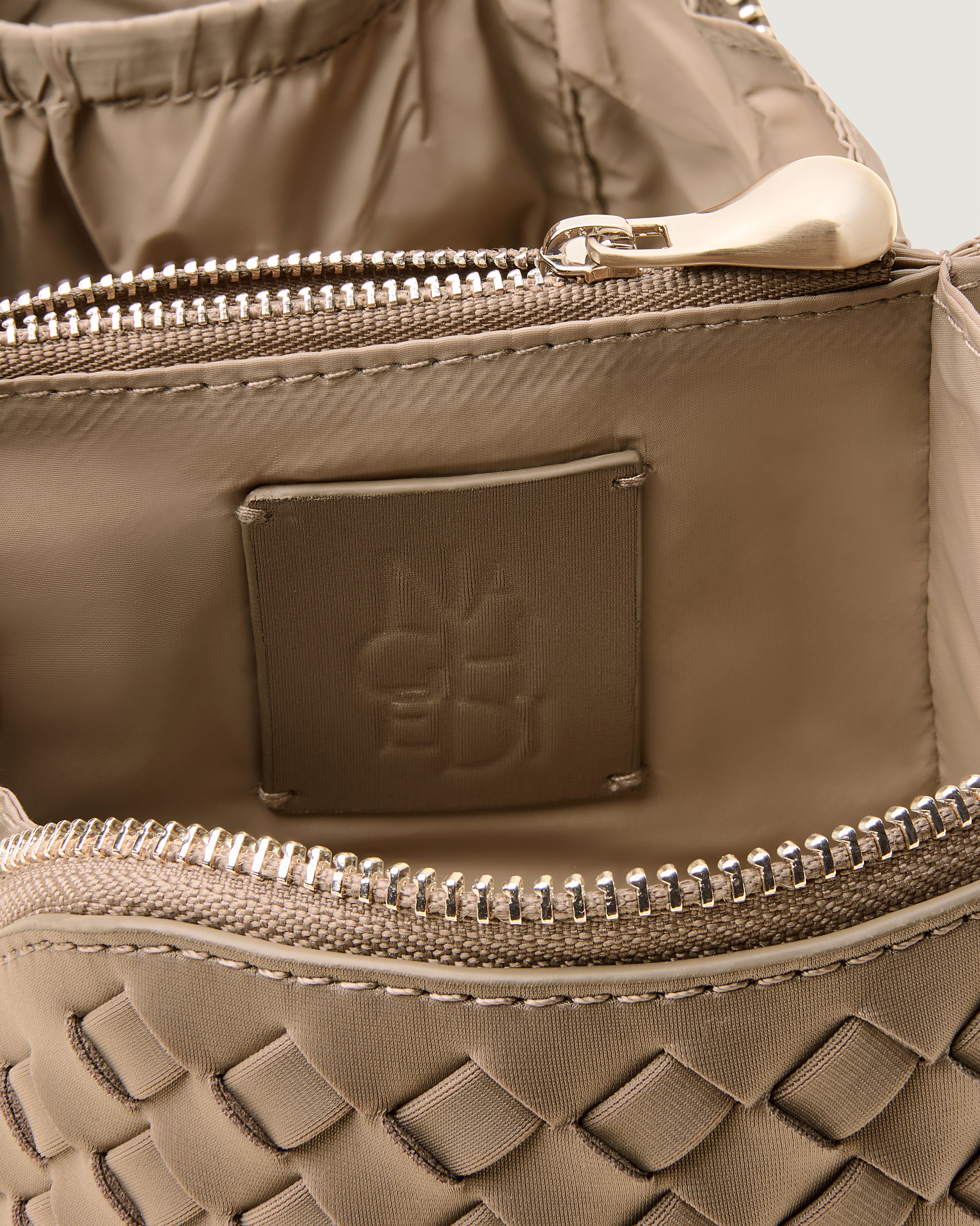 Close-up of stamped NAGHEDI logo, interior pocket and wipe-clean nylon lining in Caravan Cosmetic Case in Cashmere.
