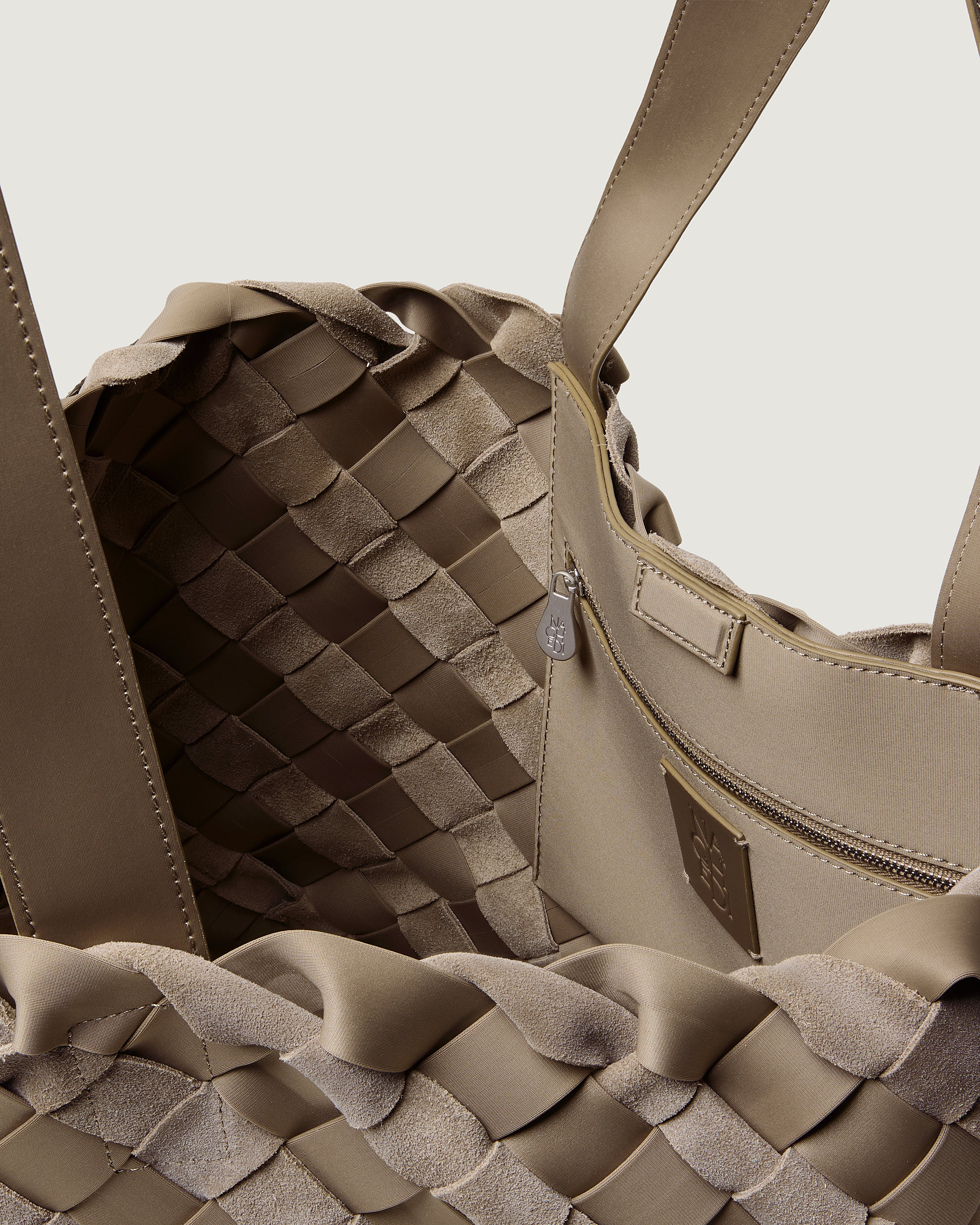 Close-up of a handwoven suede and neoprene handbag in taupe, showing the interlaced texture of the exterior, and zippered pocket.