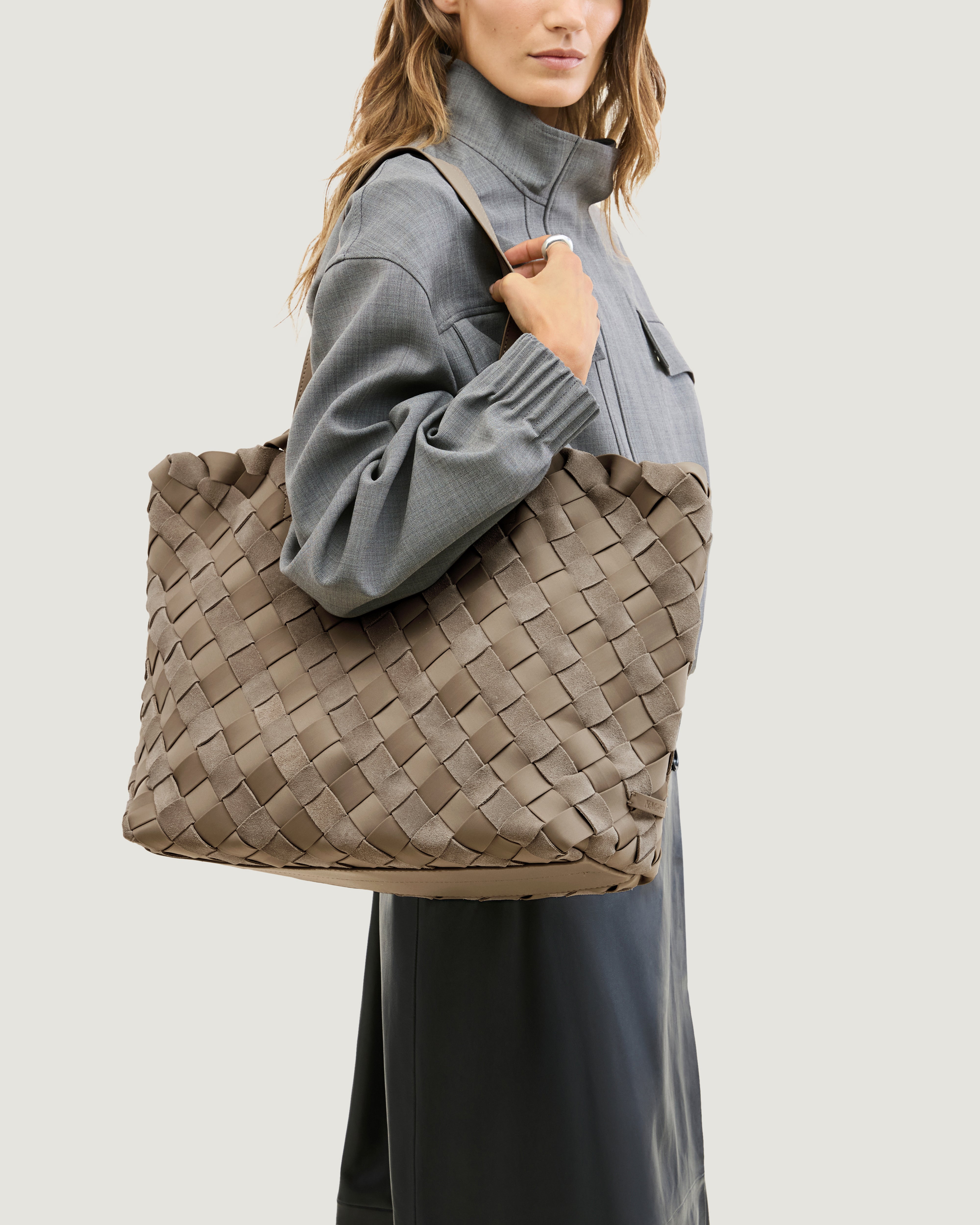 A model wearing large handwoven suede and neoprene tote bag in taupe brown with dual top handles.