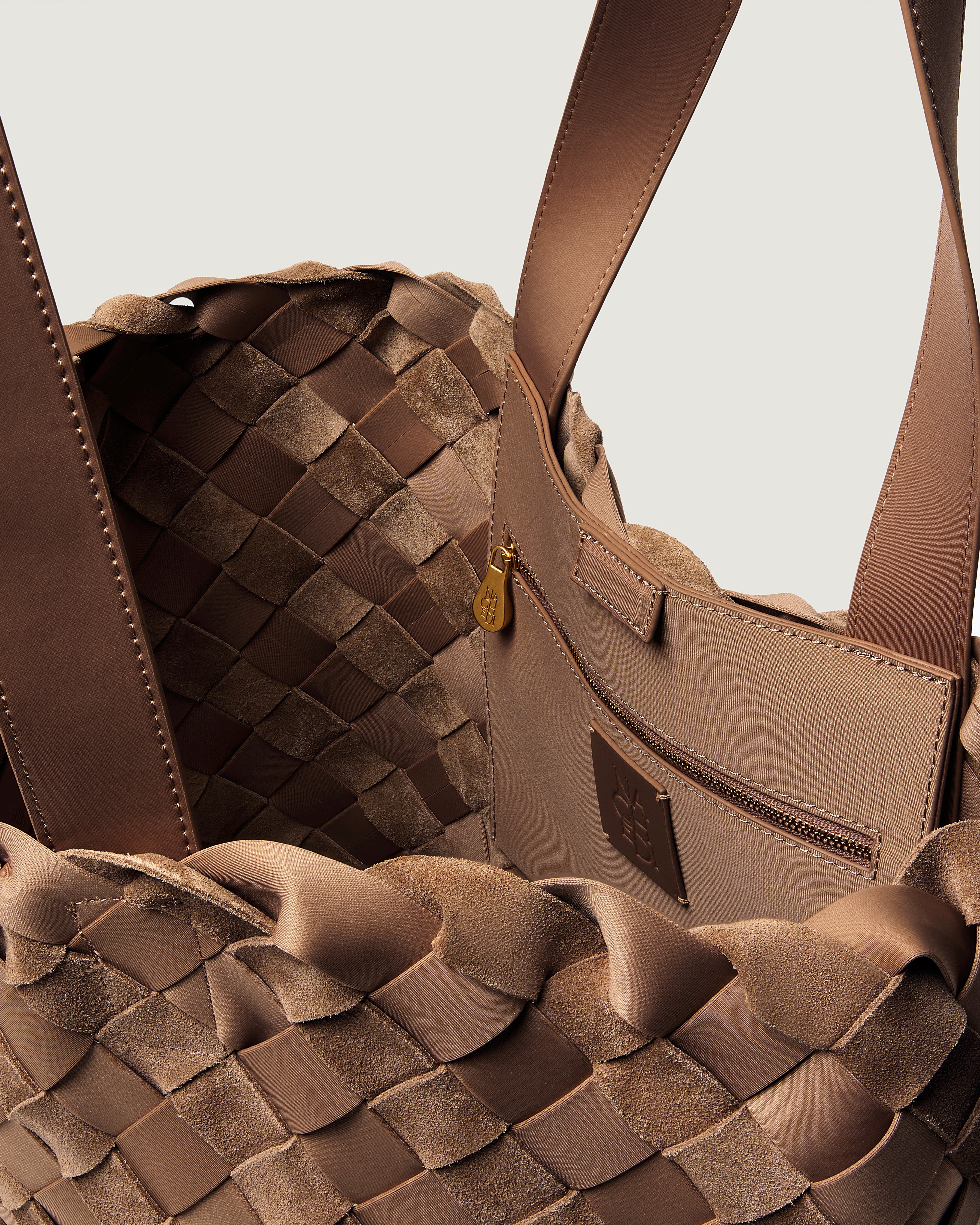 Close-up of a handwoven suede and neoprene handbag in warm taupe-brown tones, showing the interlaced exterior, interior zip pocket.