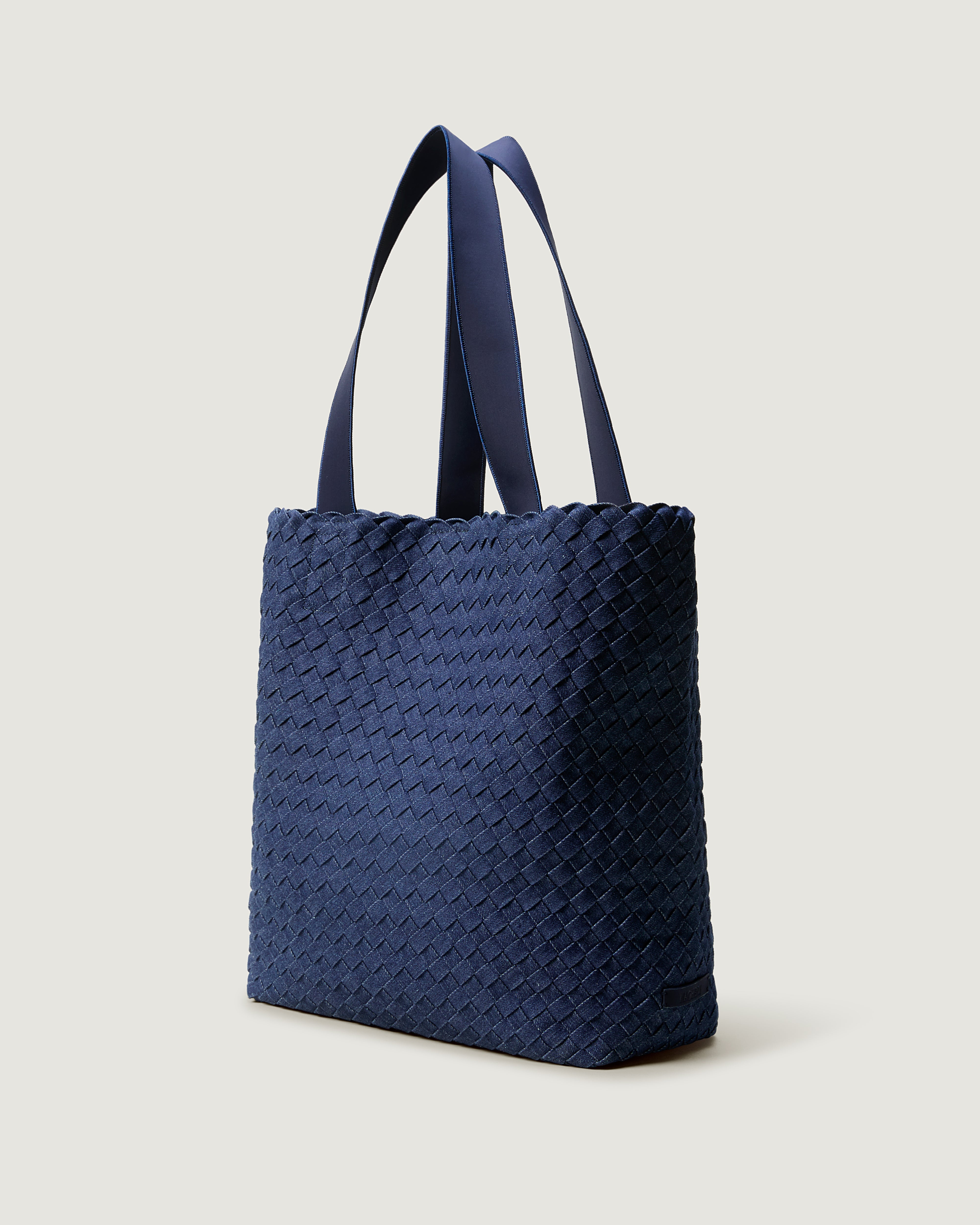 Como Tote in Denim shown from a side angle, highlighting its handwoven denim construction and open top with magnetic snap closure.