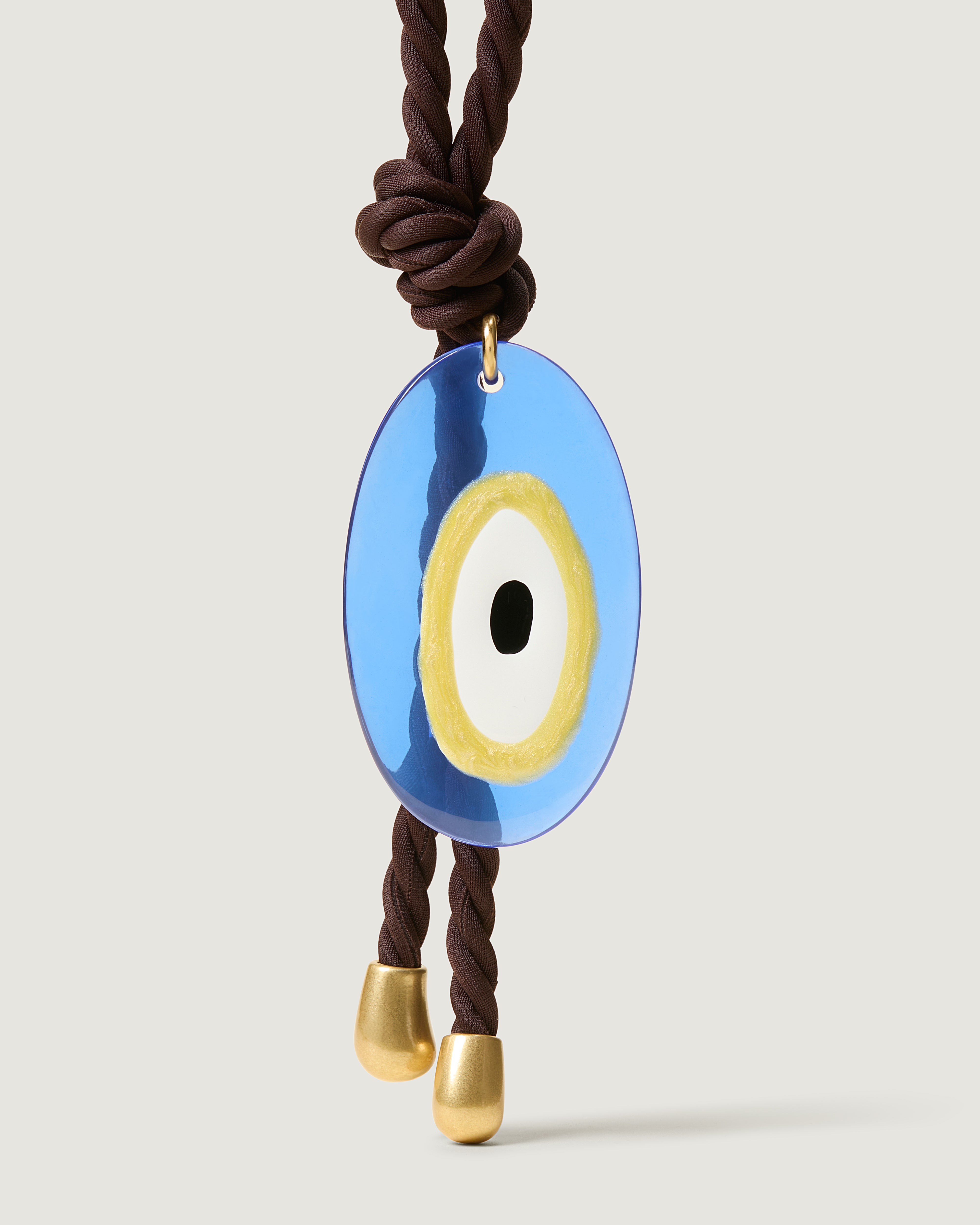 Close up of the Evil Eye Bag Charm in Chocolate. Highlighting the Evil Eye pendant and brushed gold hardware tips.