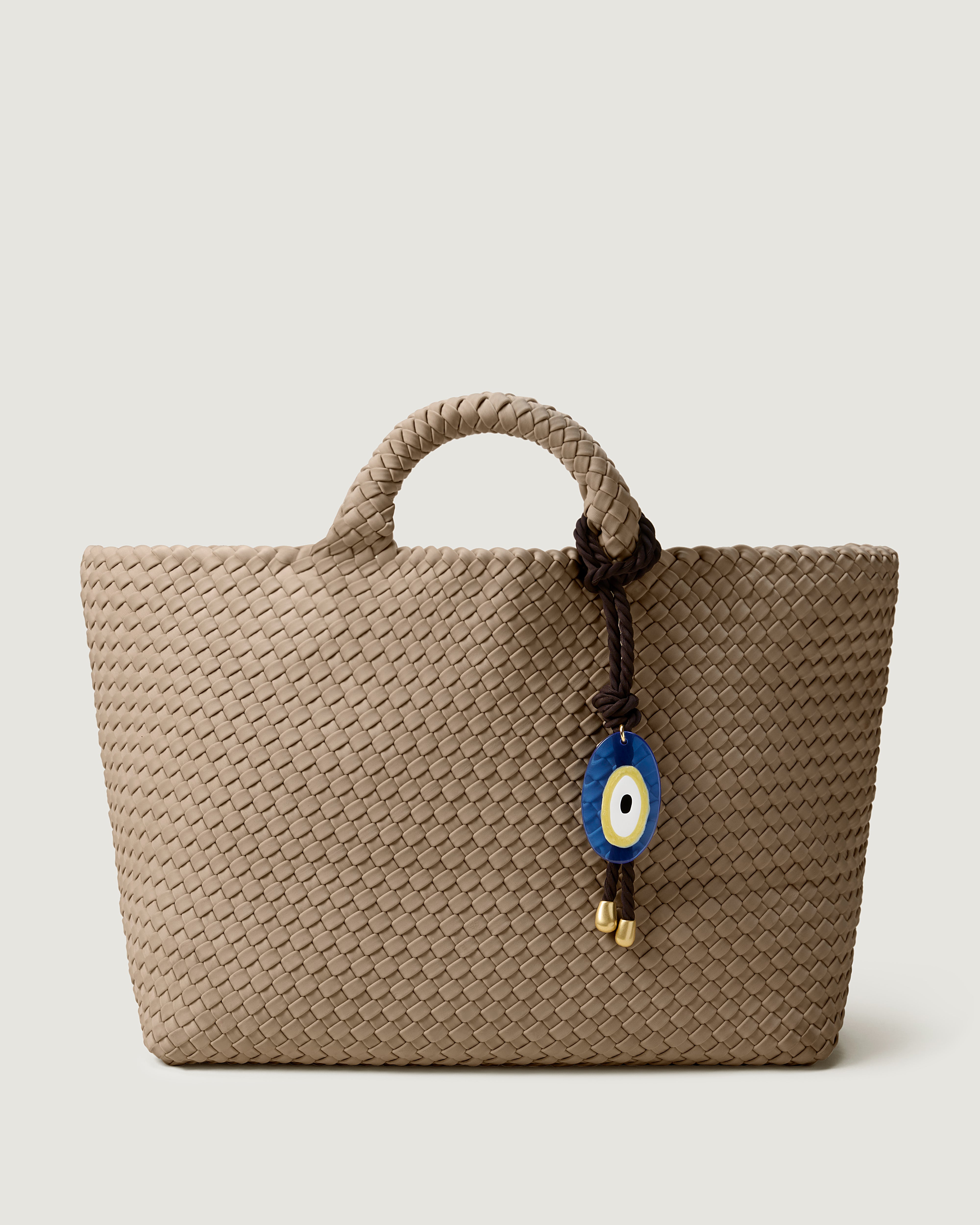 St. Barths Tote in Cashmere, a taupe tone, in handwoven neoprene, featuring an open top, and woven top handles with Chocolate Evil Eye rope bag charm.