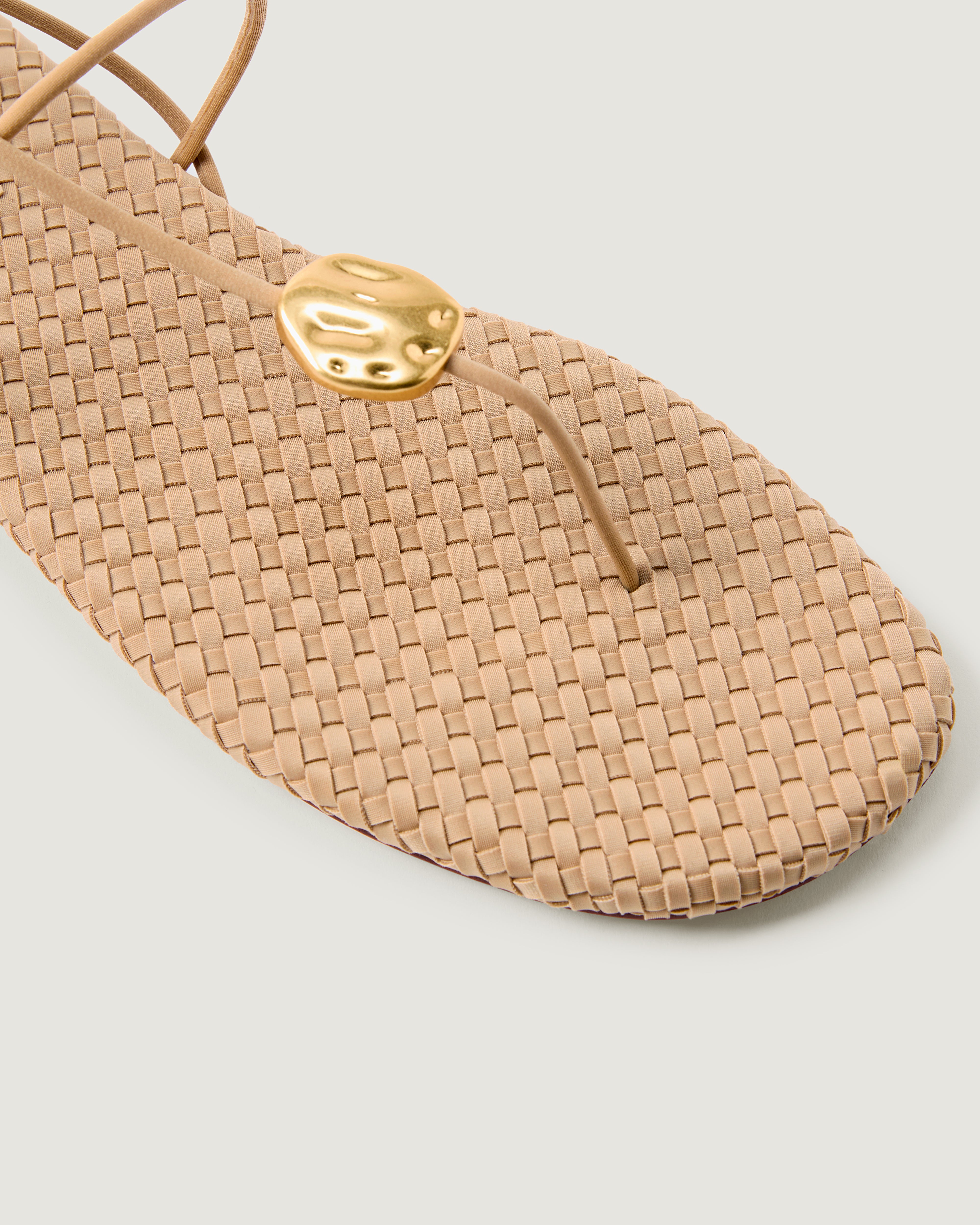 Close-up of The Gaia Sandal in Camel showing its hammered metallic disc detail.
