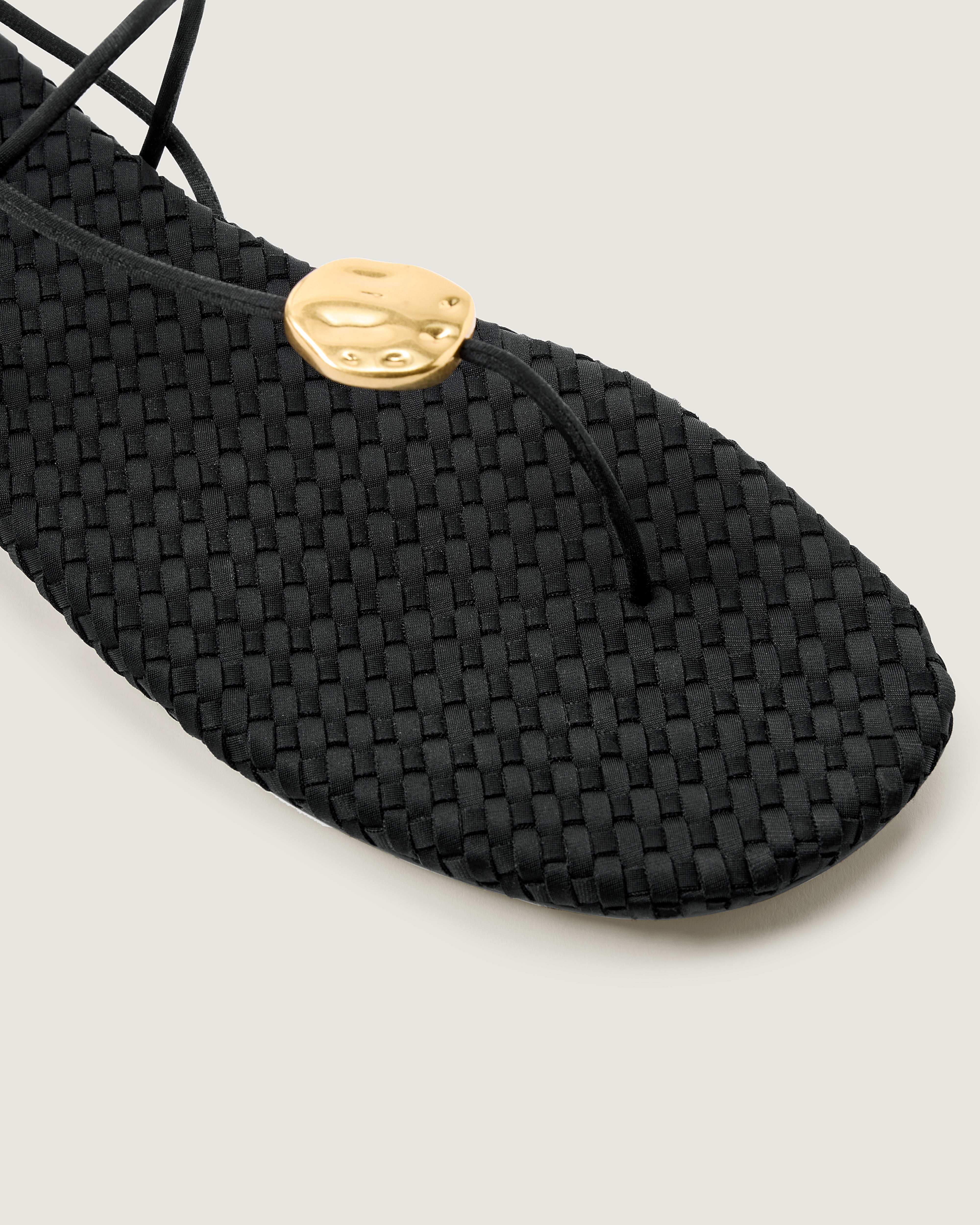 Close-up of The Gaia Sandal in Onyx showing its hammered metallic disc detail.
