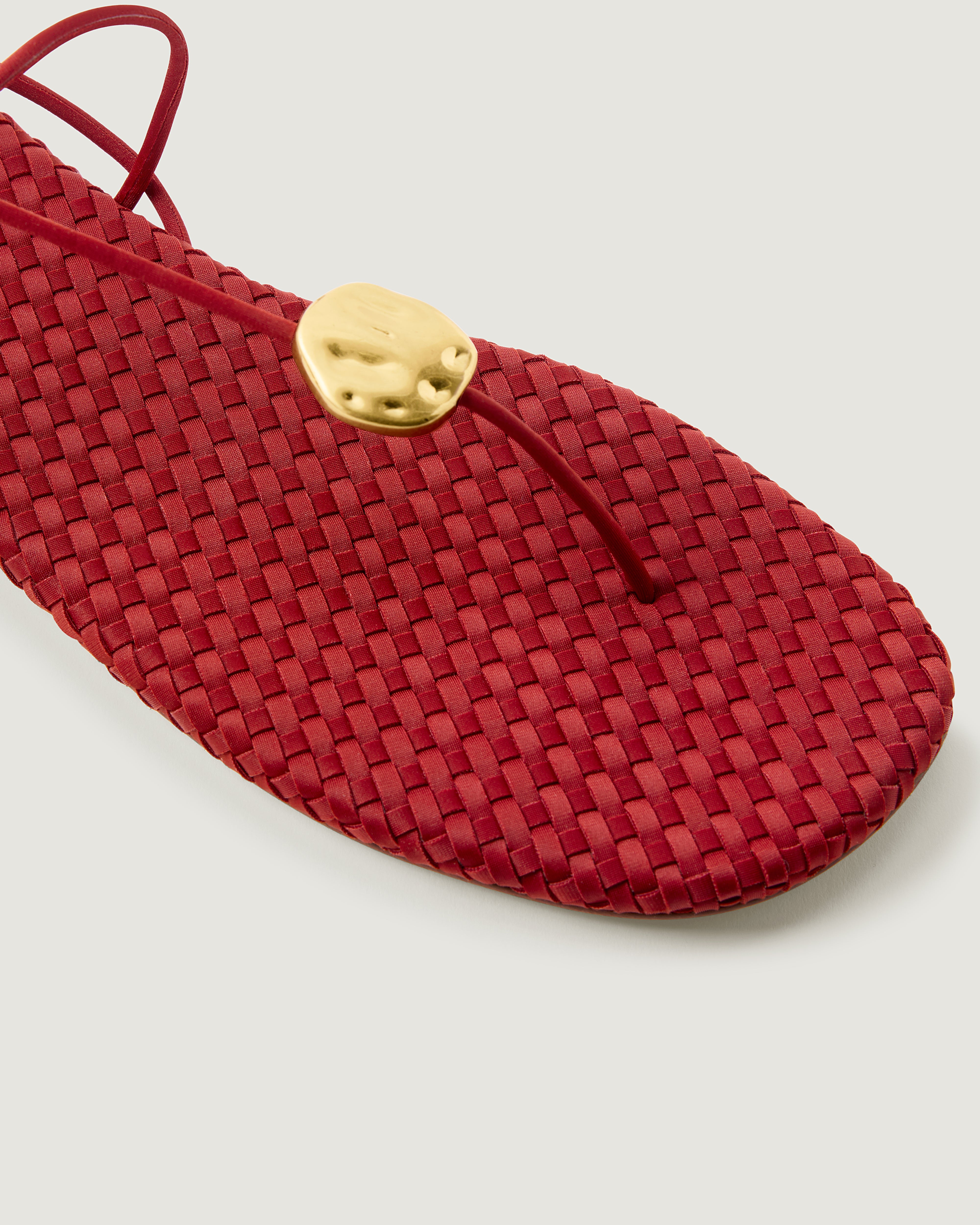 Close-up of The Gaia Sandal in Rosso showing its hammered metallic disc detail.
