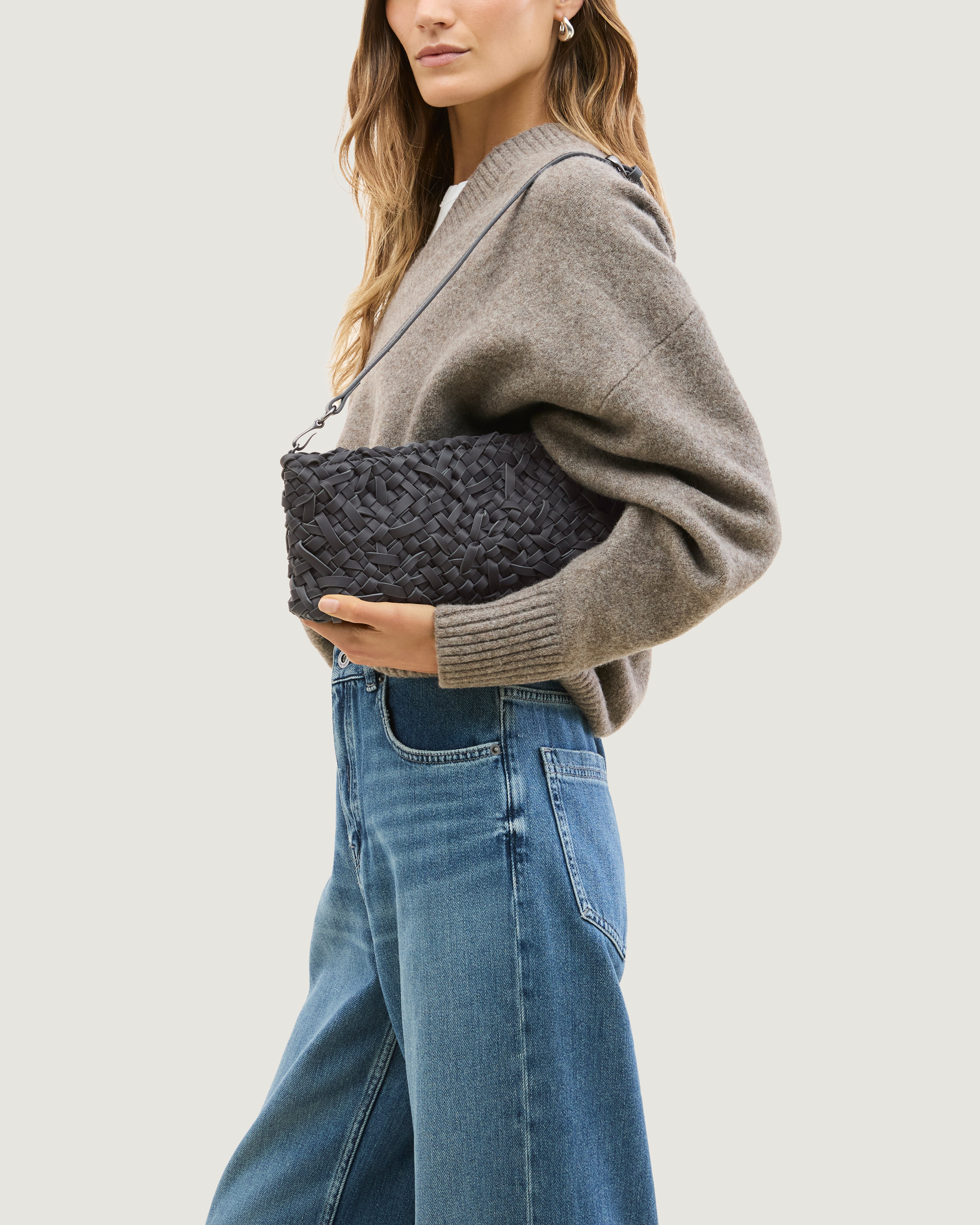 Model wearing handwoven neoprene shoulder bag in ash gray color with a crosshatch nest weave pattern and silver hardware over her shoulder