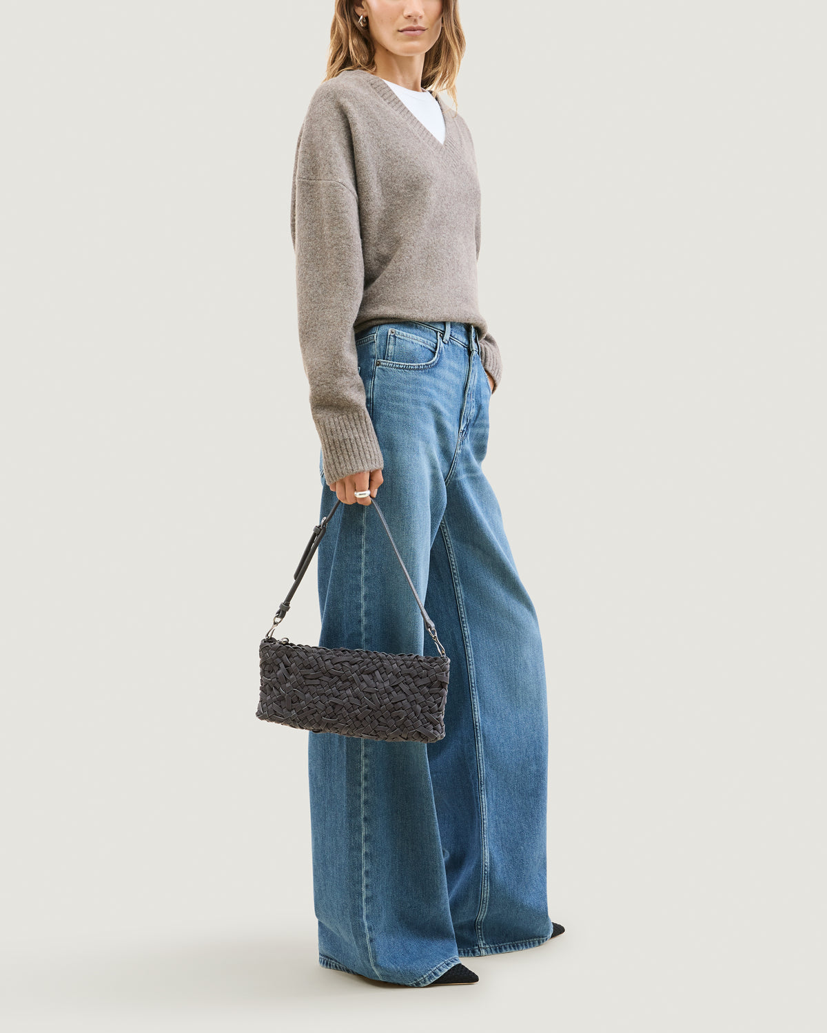 Model holding handwoven neoprene shoulder bag in ash gray color with a crosshatch nest weave pattern and silver hardware in front of her body.