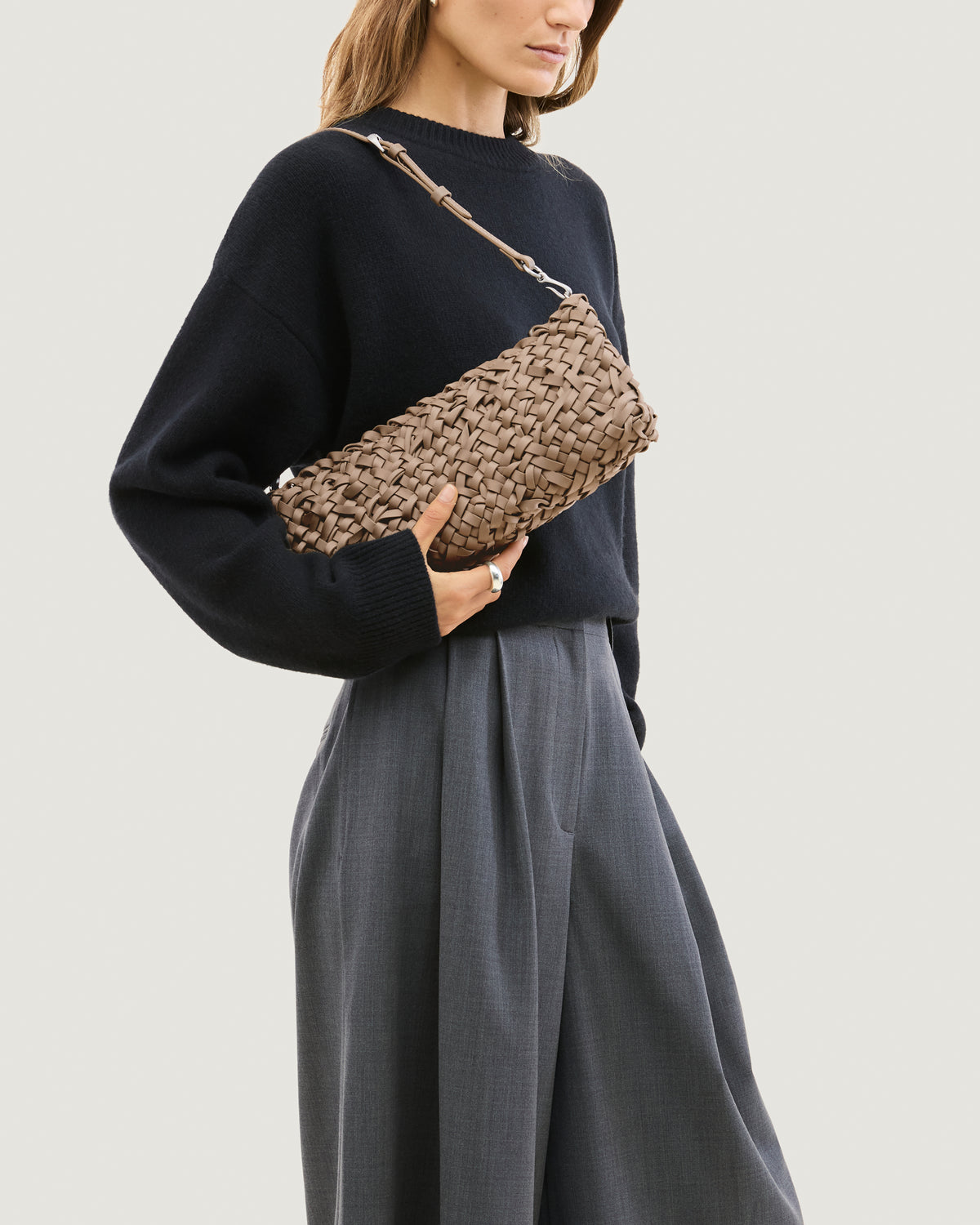 Model wearing handwoven neoprene shoulder bag in cool taupe color with a crosshatch nest weave pattern and silver hardware over her shoulder