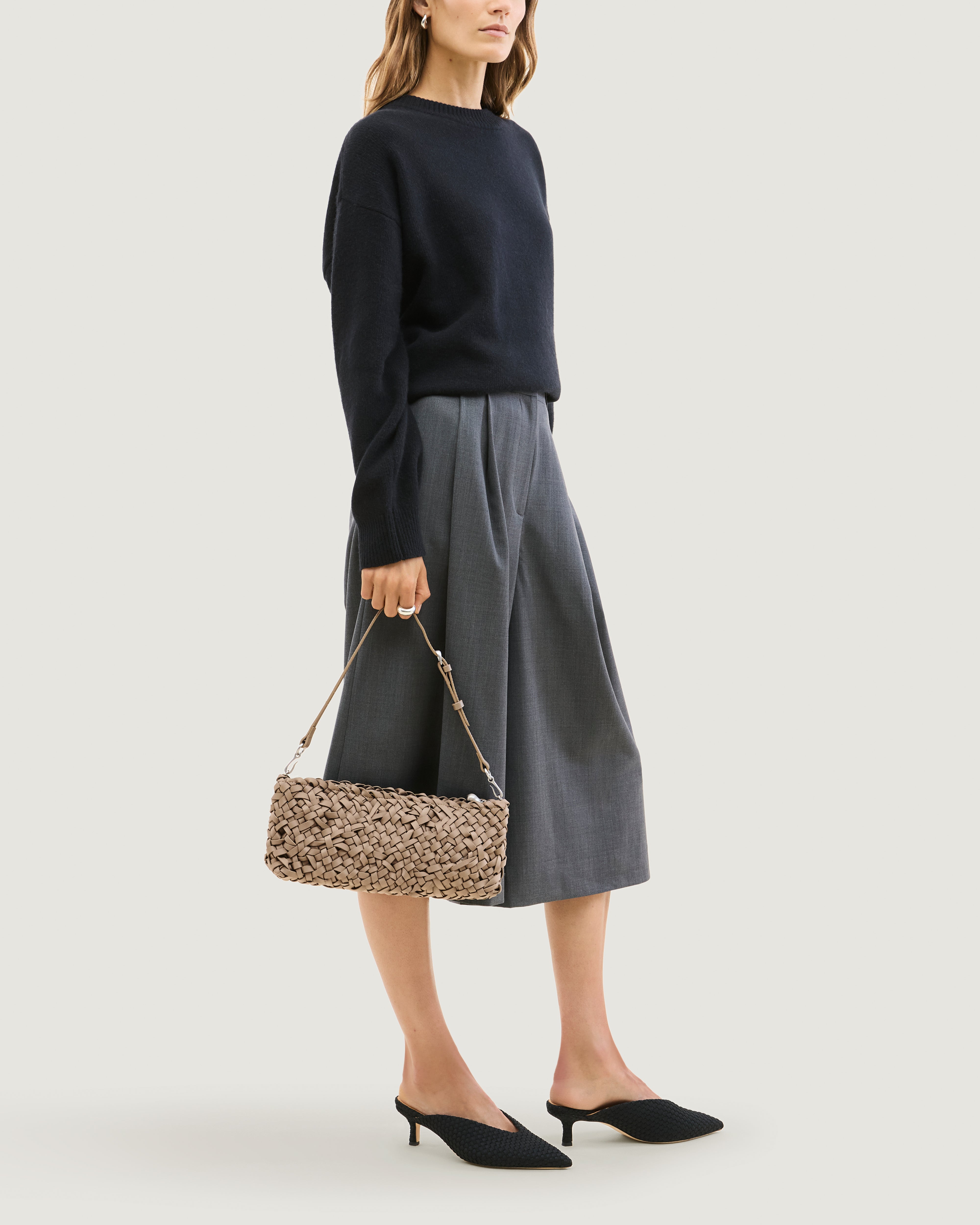 Model holding handwoven neoprene shoulder bag in cool taupe color with a crosshatch nest weave pattern and silver hardware in front of her body.