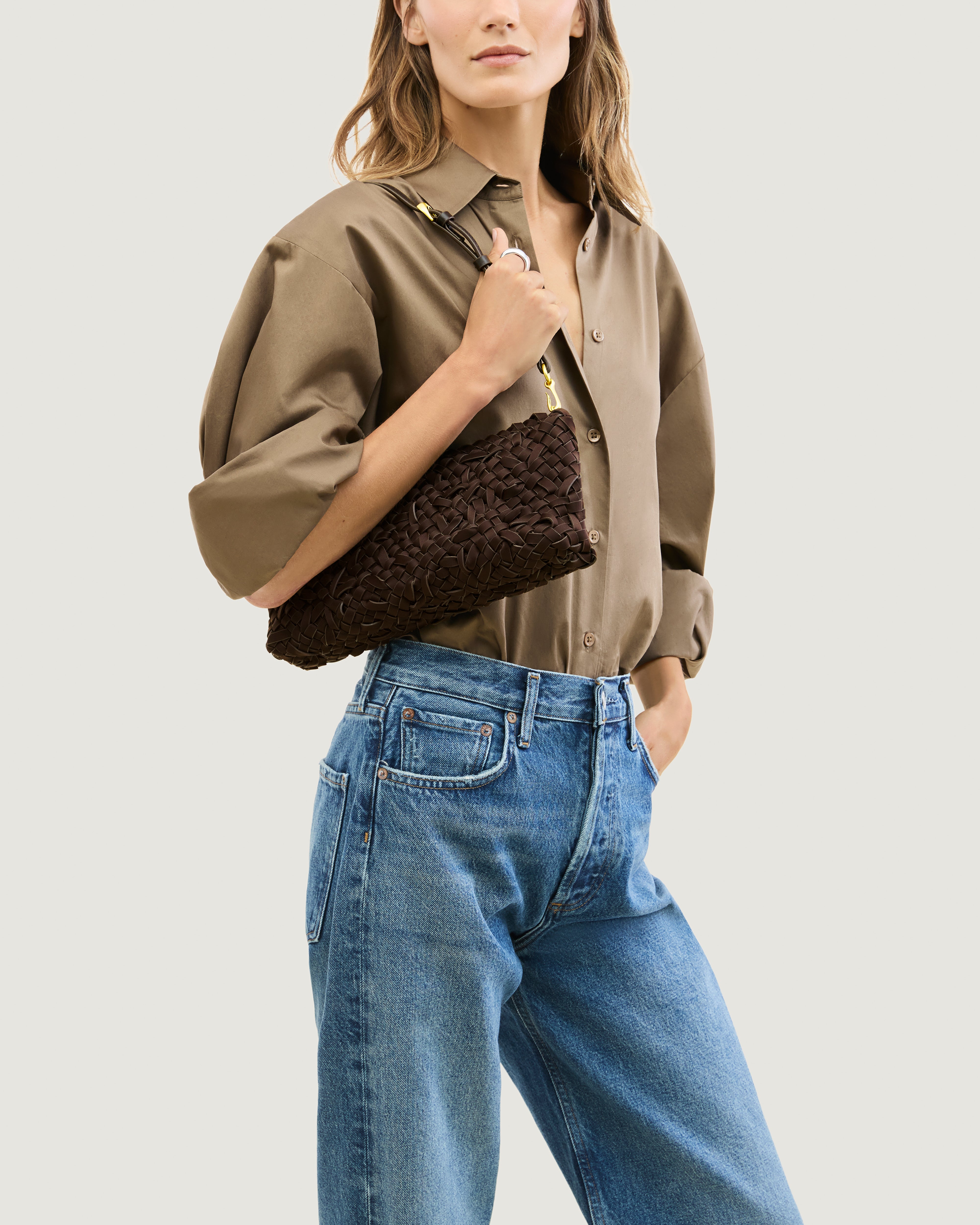 Model wearing handwoven neoprene shoulder bag in chocolate brown color with a crosshatch nest weave pattern and gold hardware over her shoulder