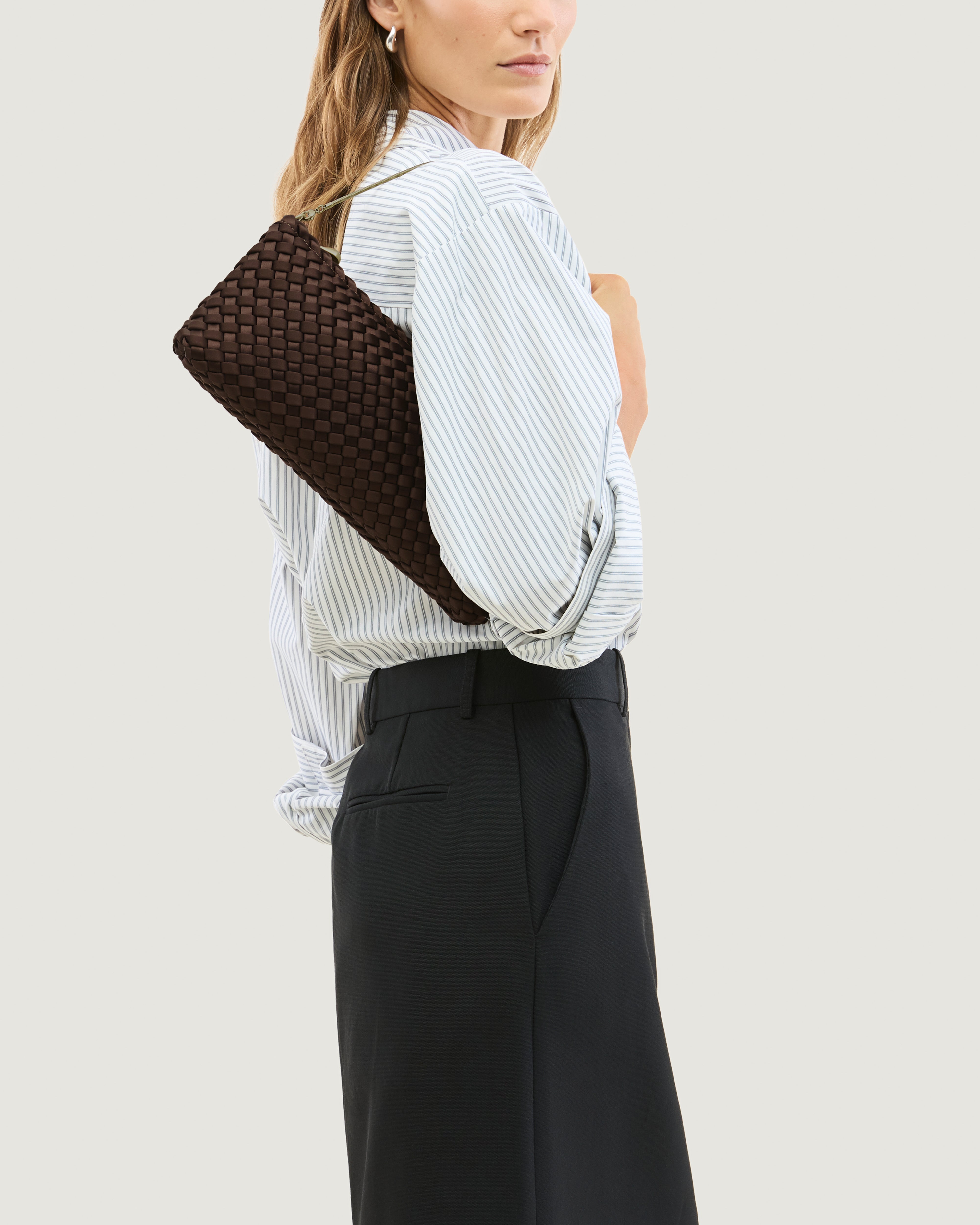 Model holding a handwoven satin neoprene shoulder bag in chocolate brown with a thin gold metal chain strap.