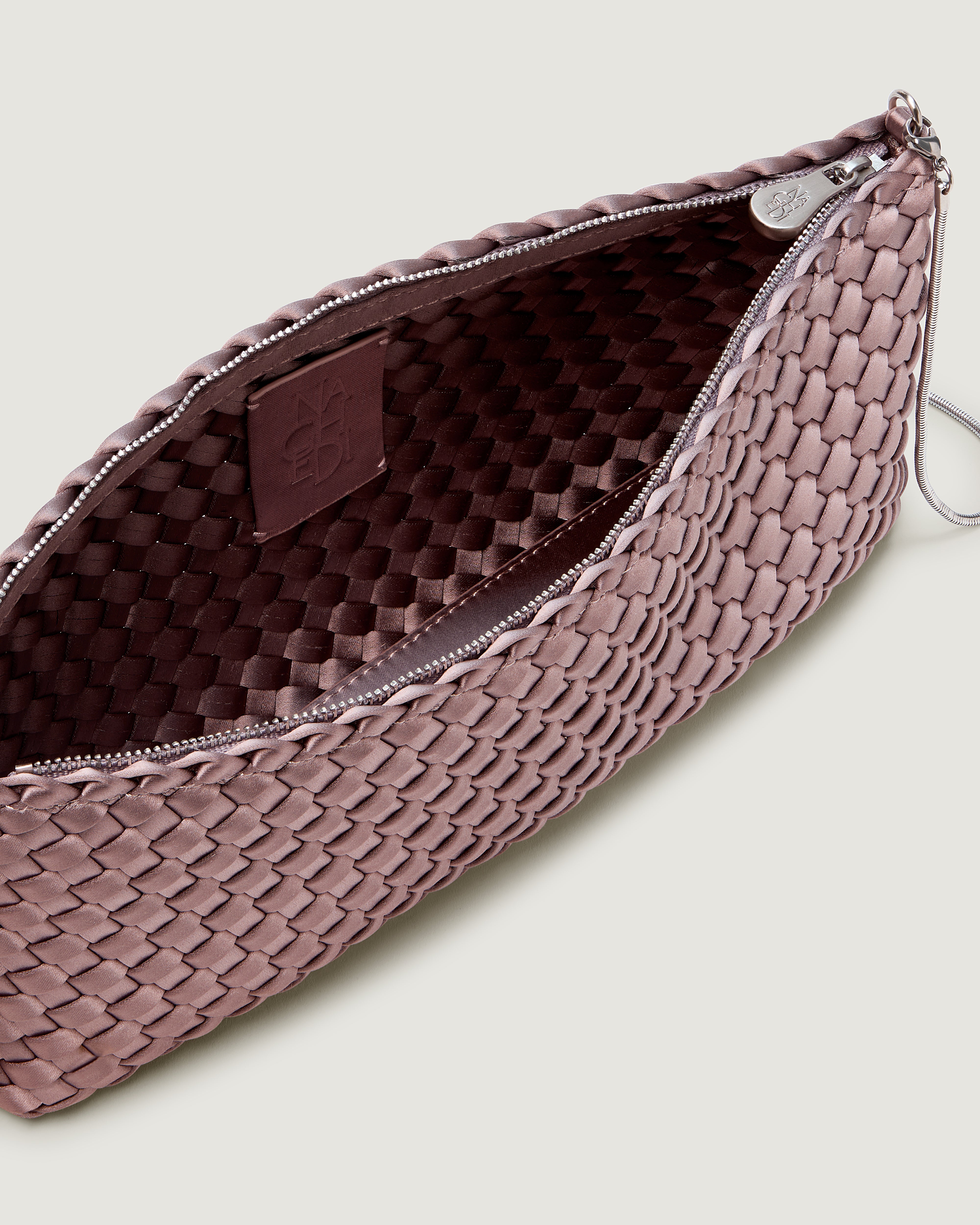 An interior shot of a handwoven satin neoprene shoulder bag in lavender with a thin silver metal chain strap.