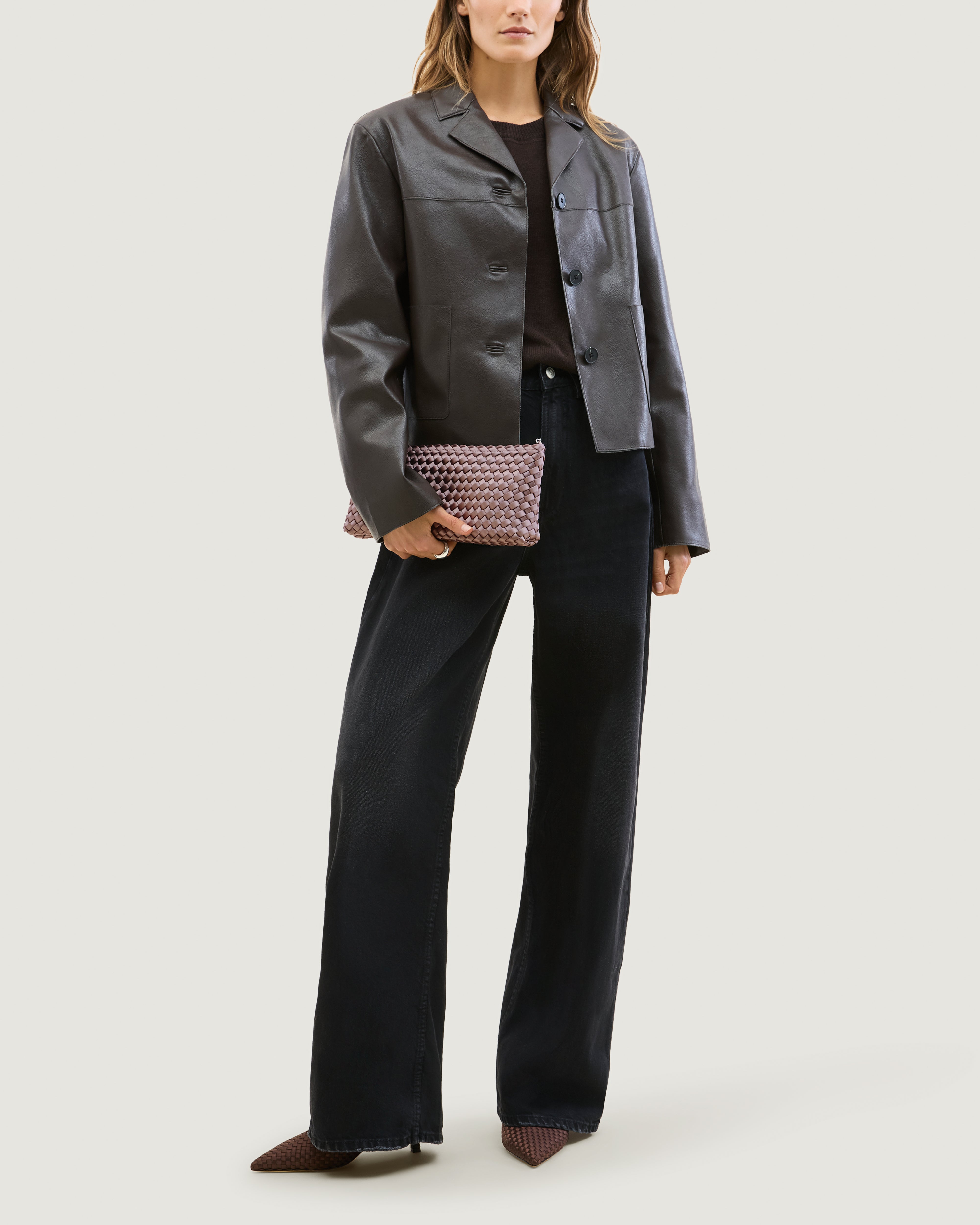 Model holding a handwoven satin neoprene shoulder bag in lavender with a thin silver metal chain strap as a clutch in front of her body.