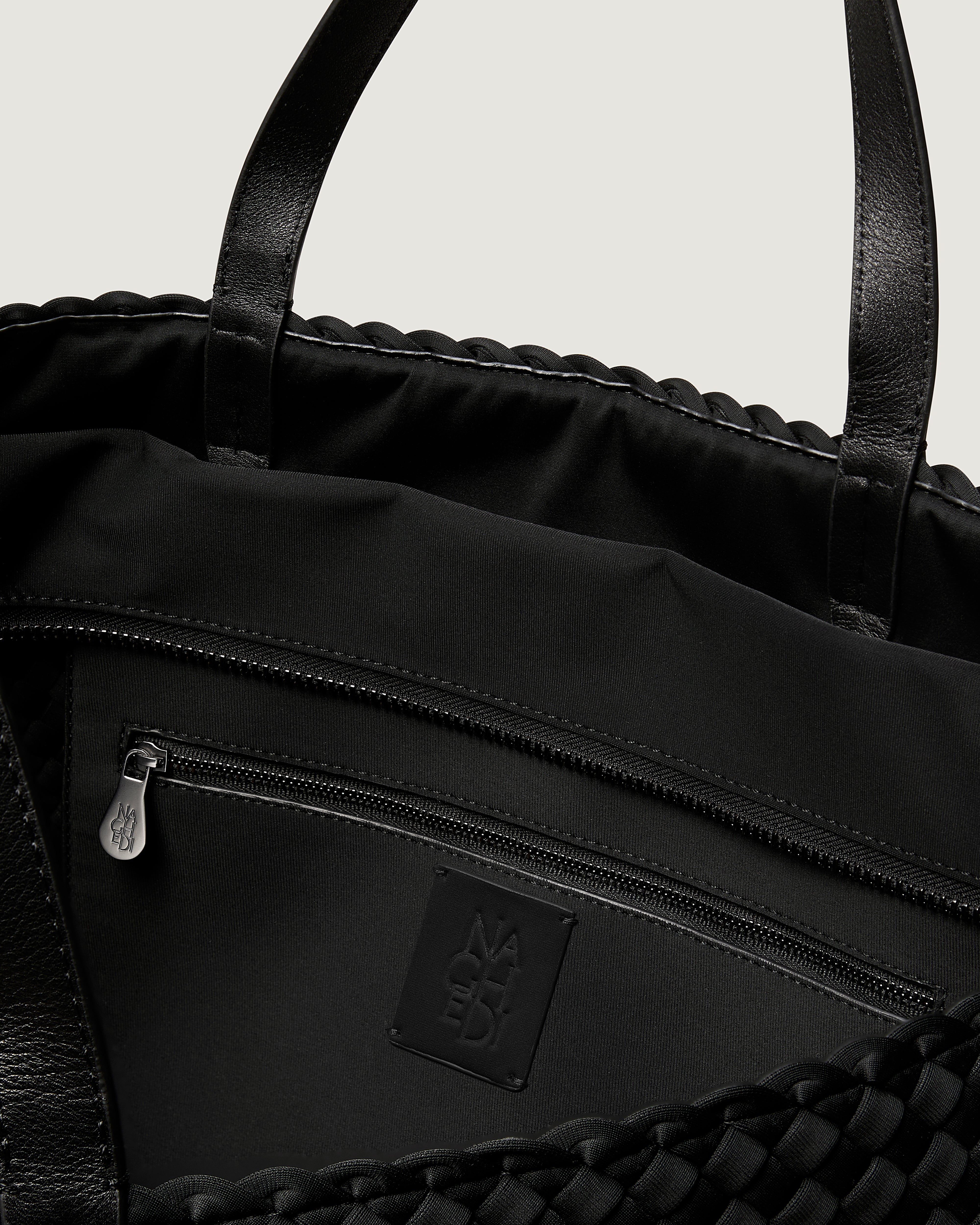 Interior close-up of Geneva Weekender in Onyx showing its top zip closure, interior pocket, and unlined interior.