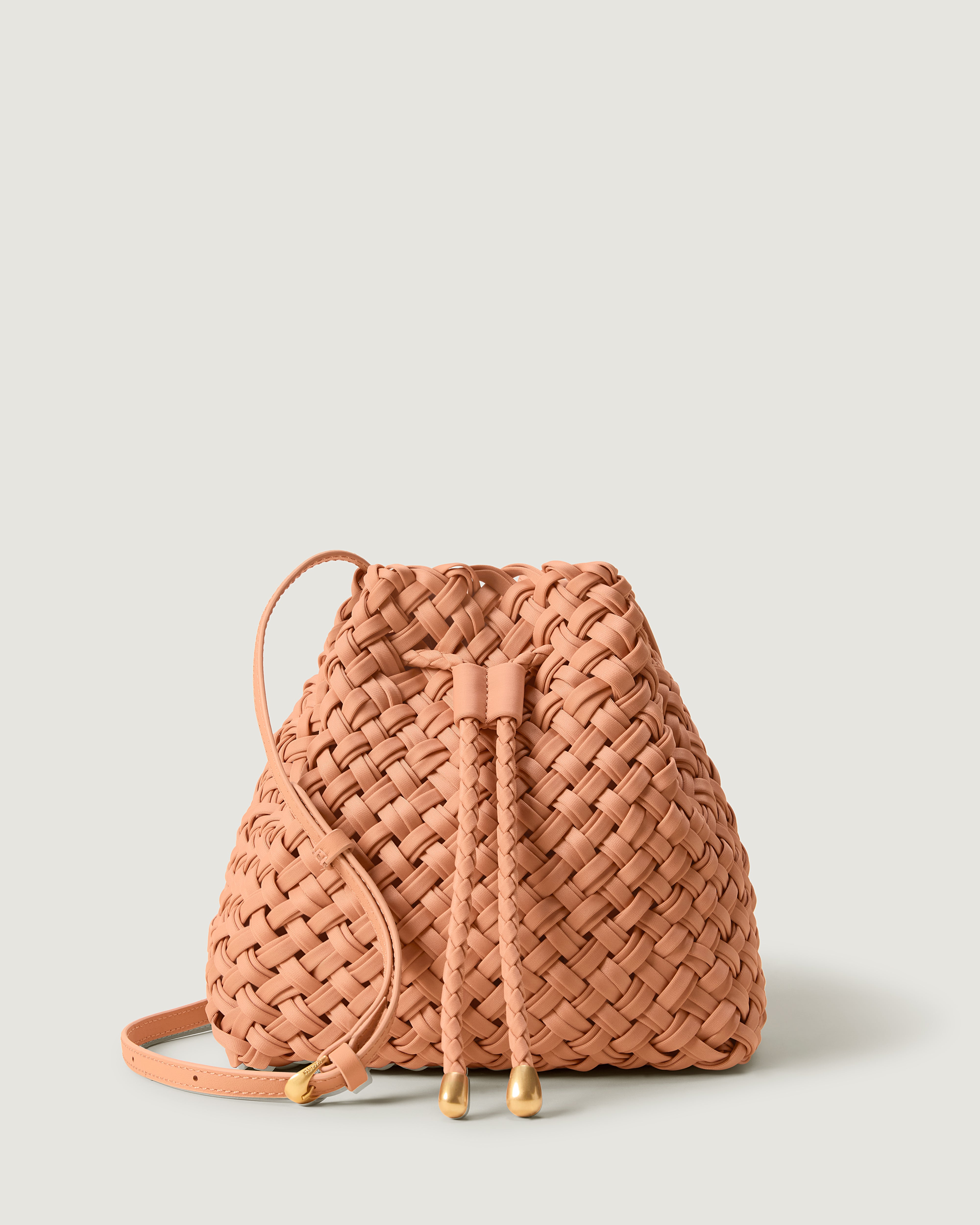 Gramercy Bucket in Etna, handwoven from doubled strands of muted coral neoprene. Featuring a drawstring closure, and adjustable leather crossbody strap.