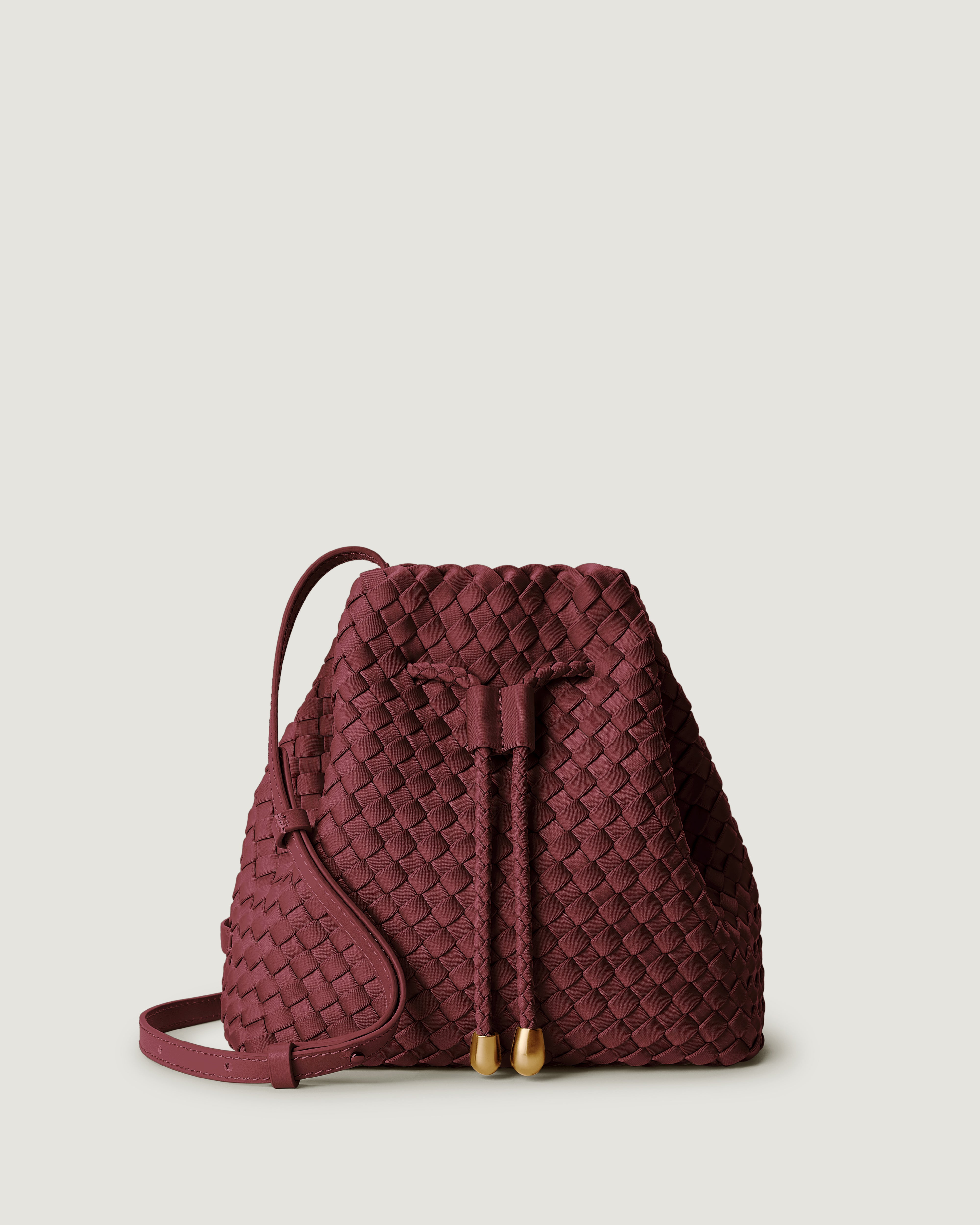 Gramercy Bucket in Bordeaux, a burgundy tone, in handwoven neoprene, featuring a drawstring closure, and adjustable leather crossbody strap.