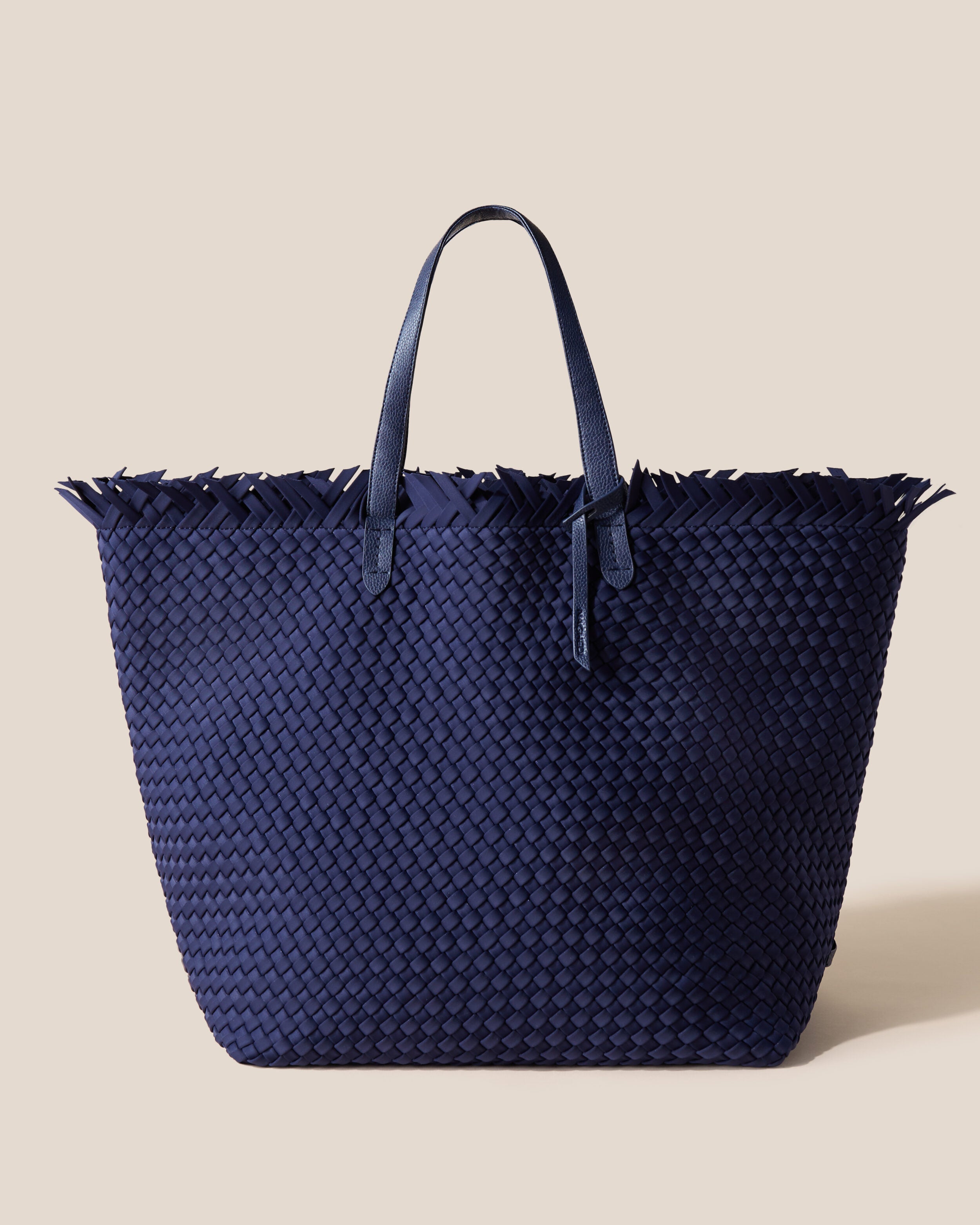 Havana  in Ink Blue, a navy blue tone, in handwoven neoprene, featuring a top zip closure, and sleek nylon webbing handles fit over the shoulder.