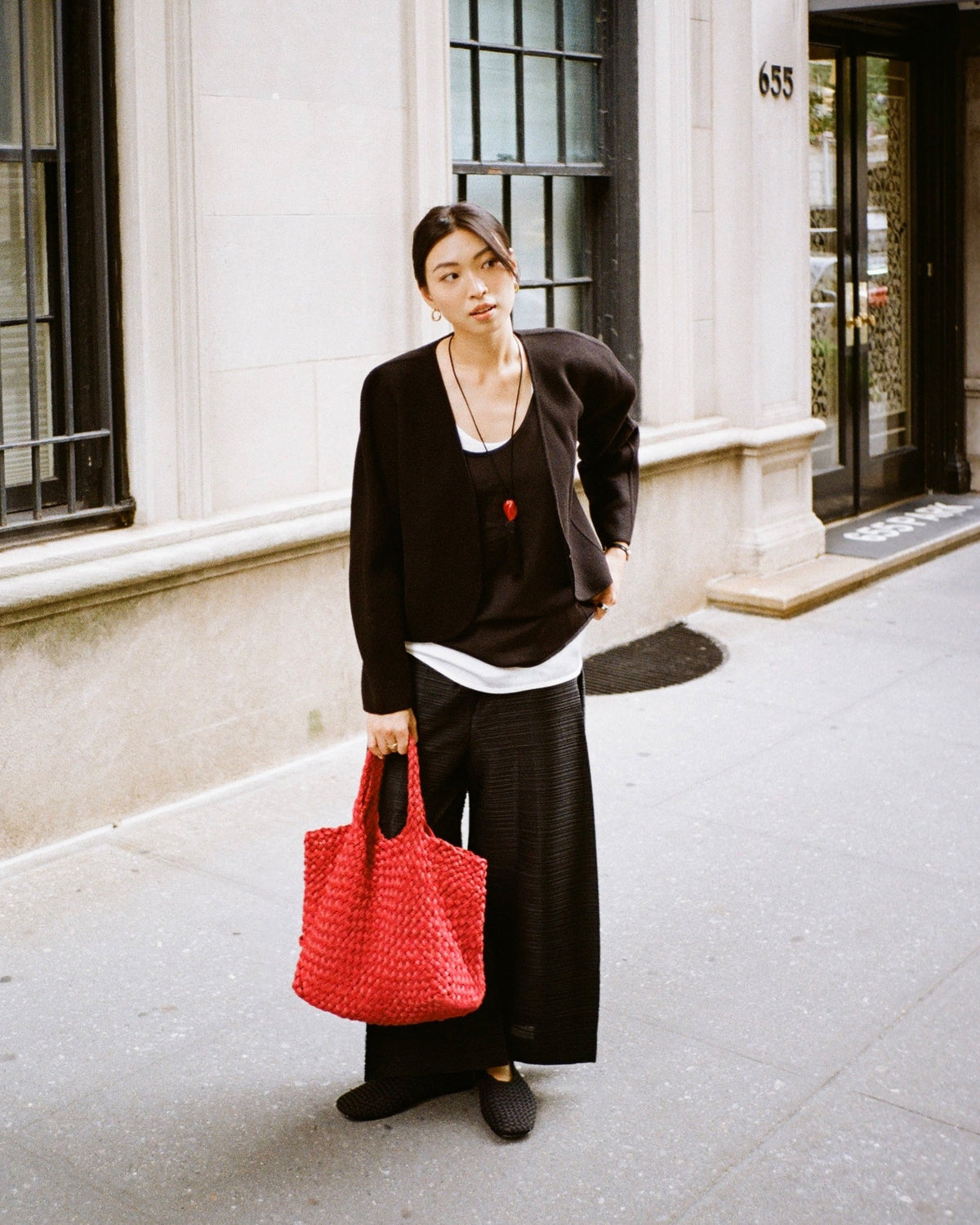 Woman holding St. Barths Medium tote in handwoven neoprene and suede in bright cherry red color at her side. Soft silhouette and relaxed structure of bag are shown