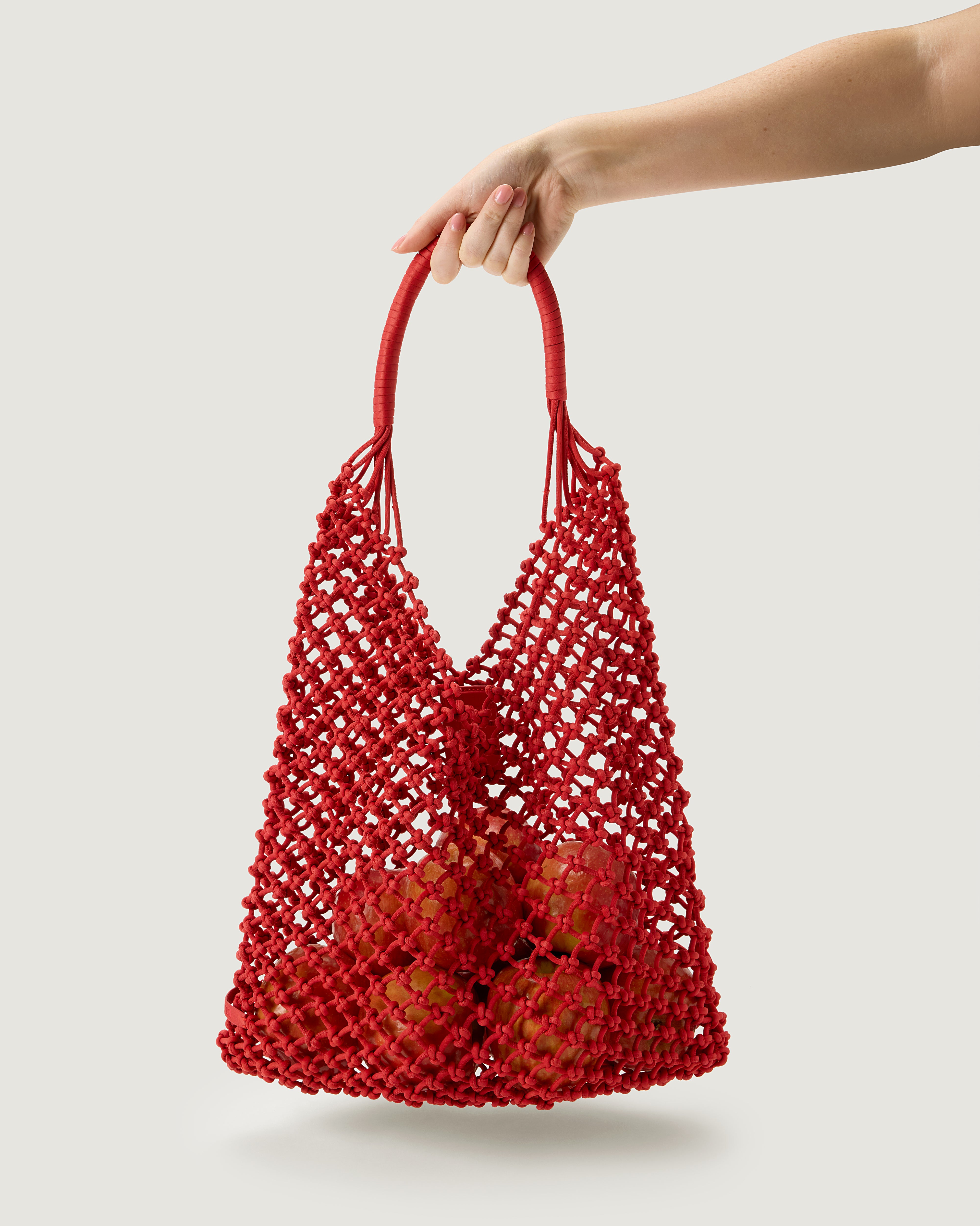 Arm holding large woven neoprene net bag in cherry red