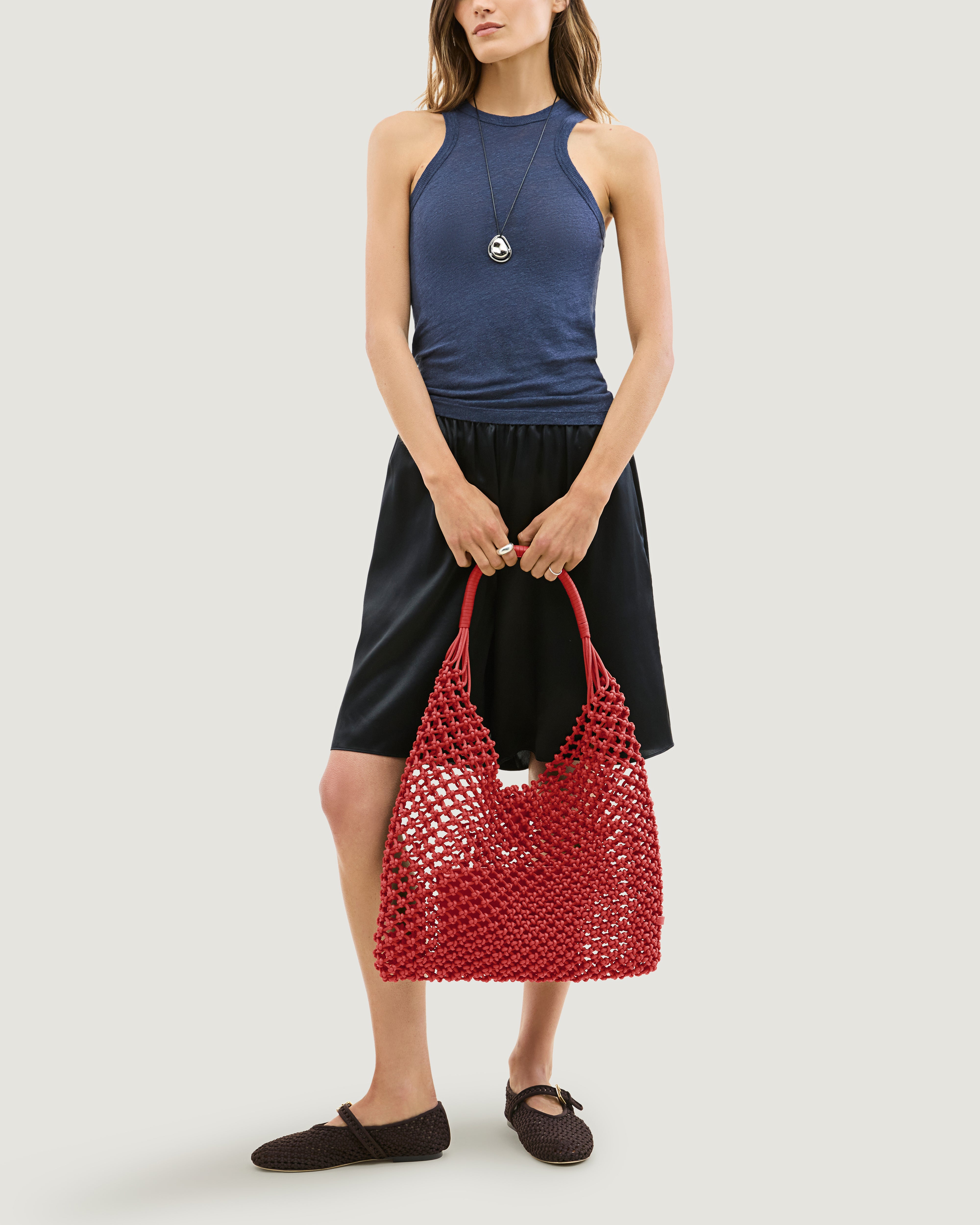 Model holding large woven neoprene net bag in cherry red in front of her