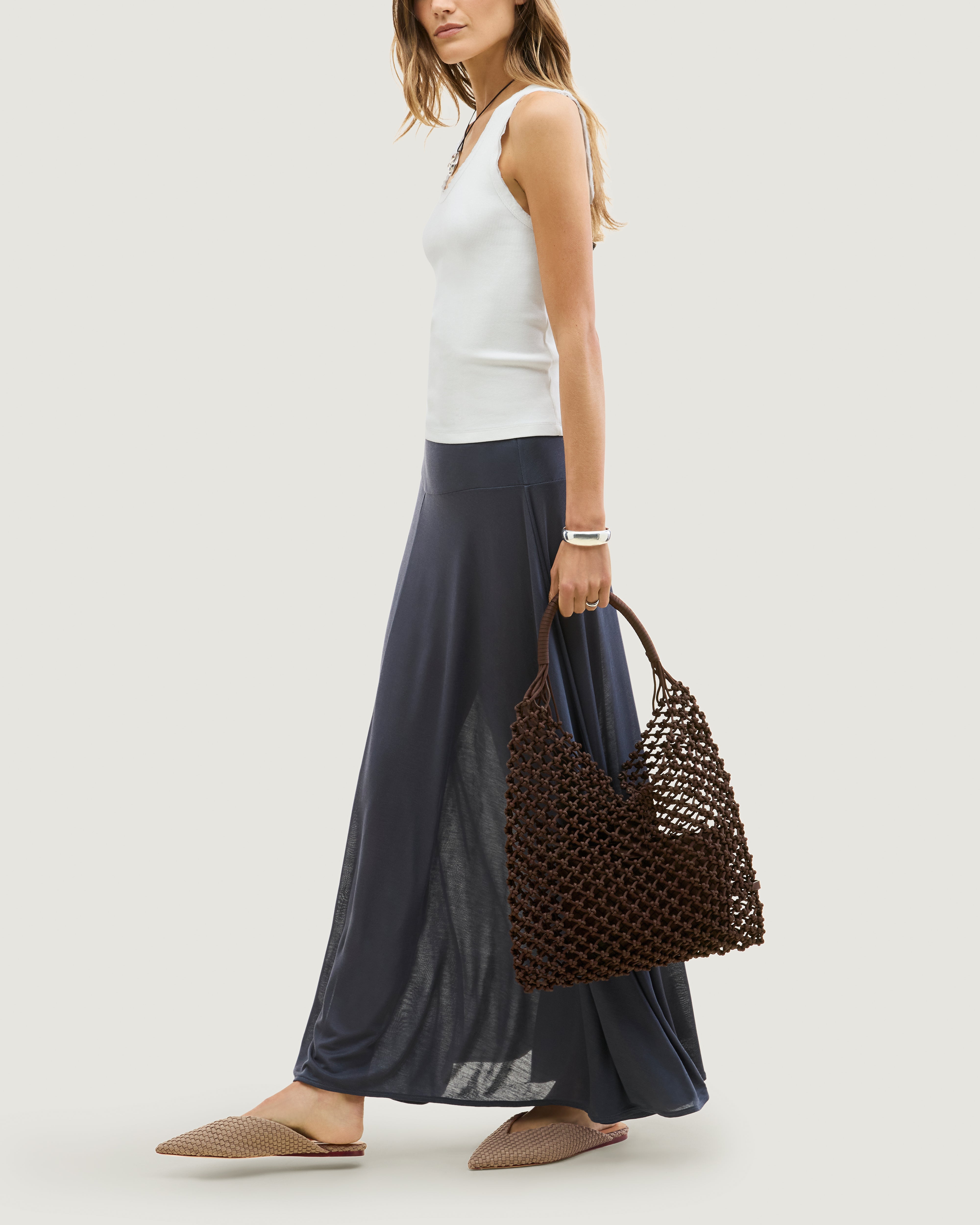Model walking holding woven neoprene net bag in chocolate brown at her side