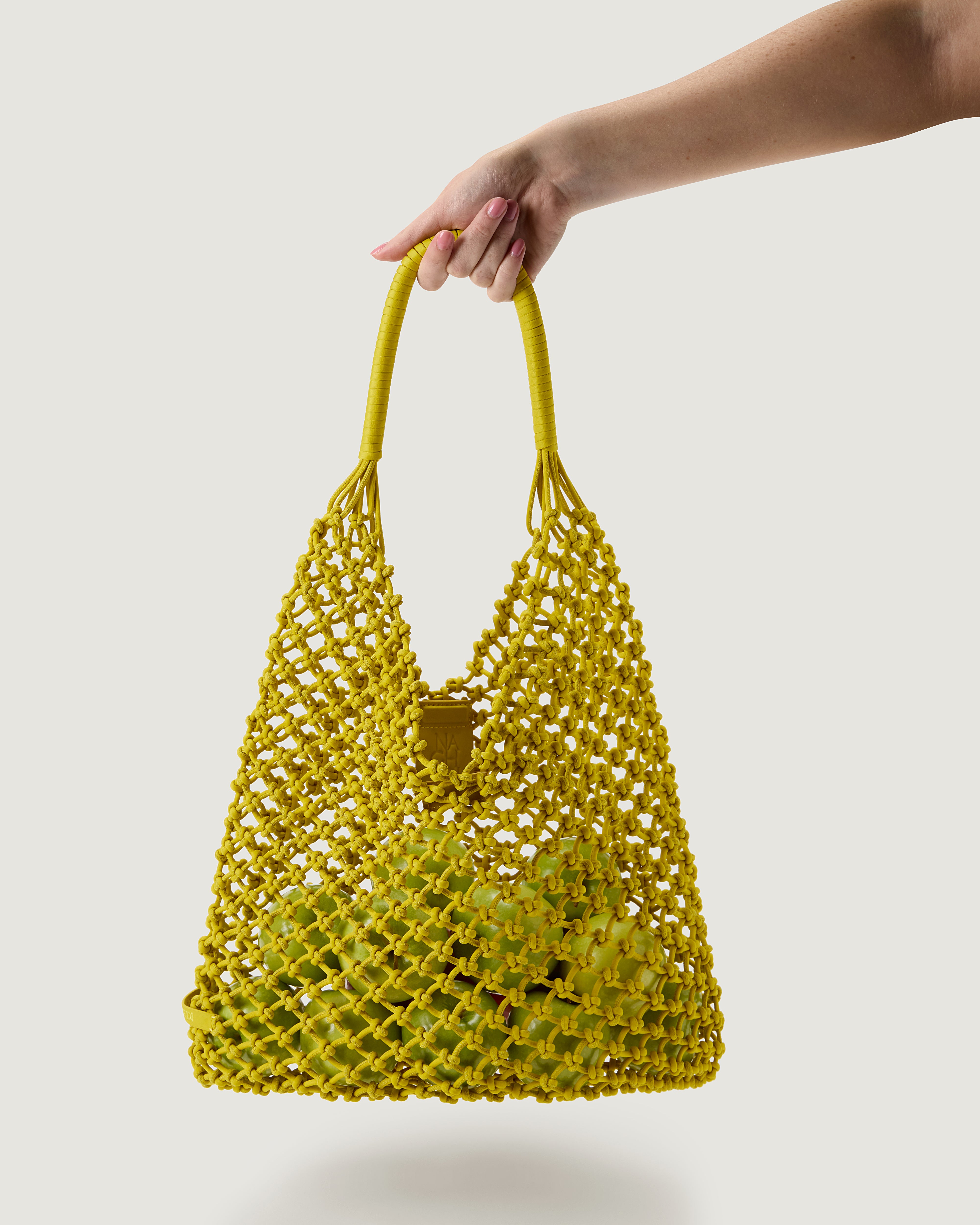 Arm holding woven neoprene net bag in golden chartreuse with fruit inside