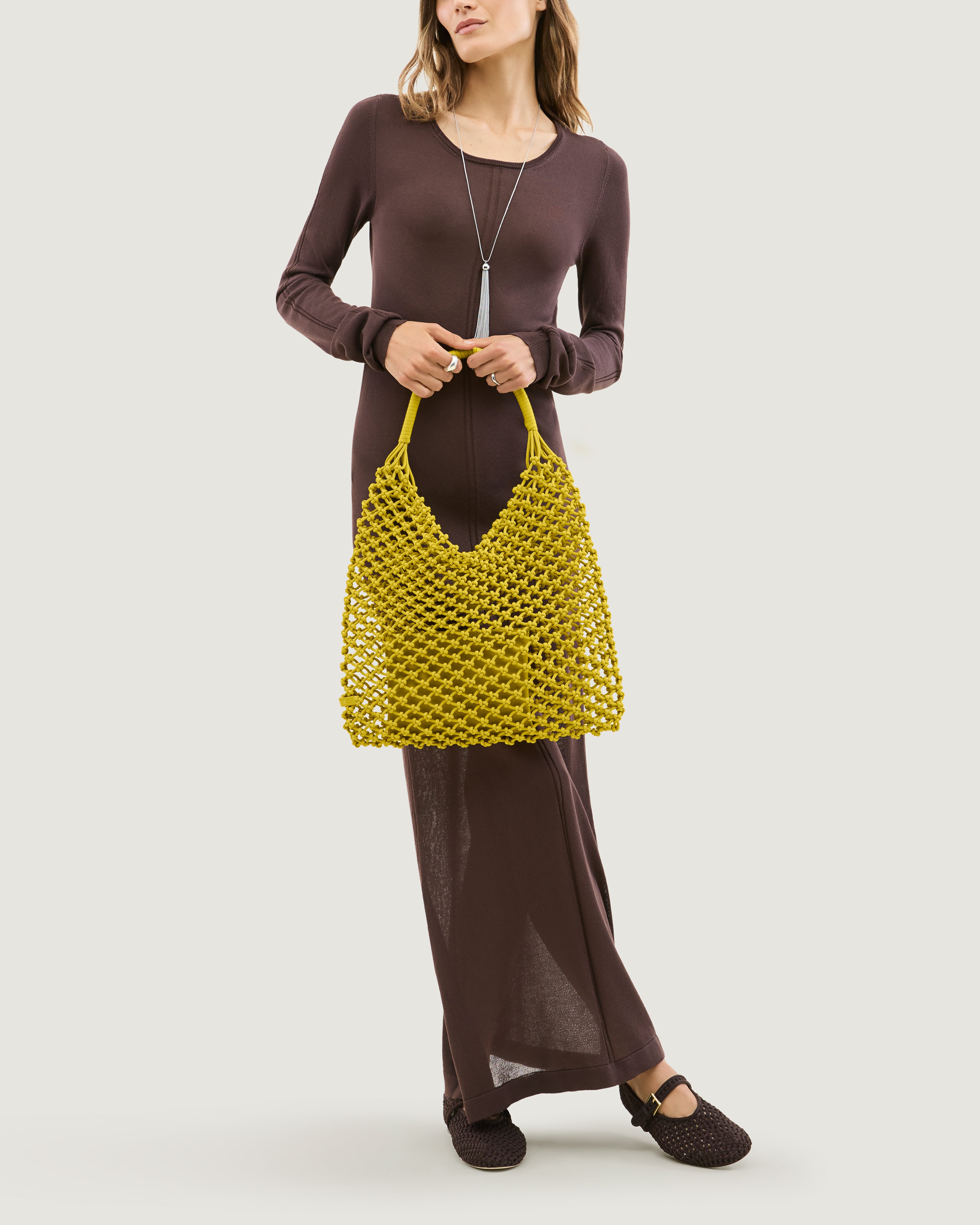 Model holding woven neoprene net bag in golden chartreuse in front of her body
