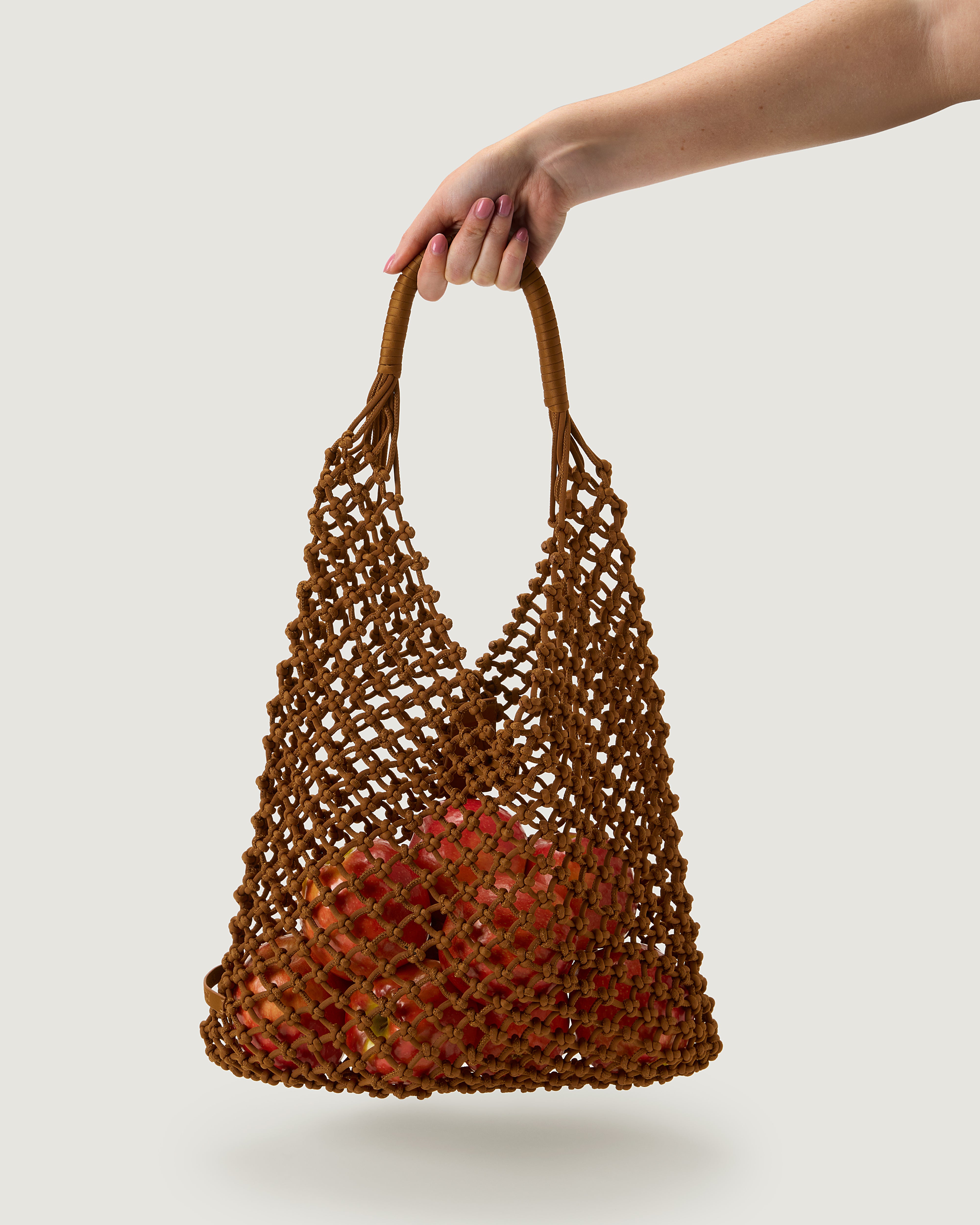 Arm holding woven net bag in saddle brown with apples inside