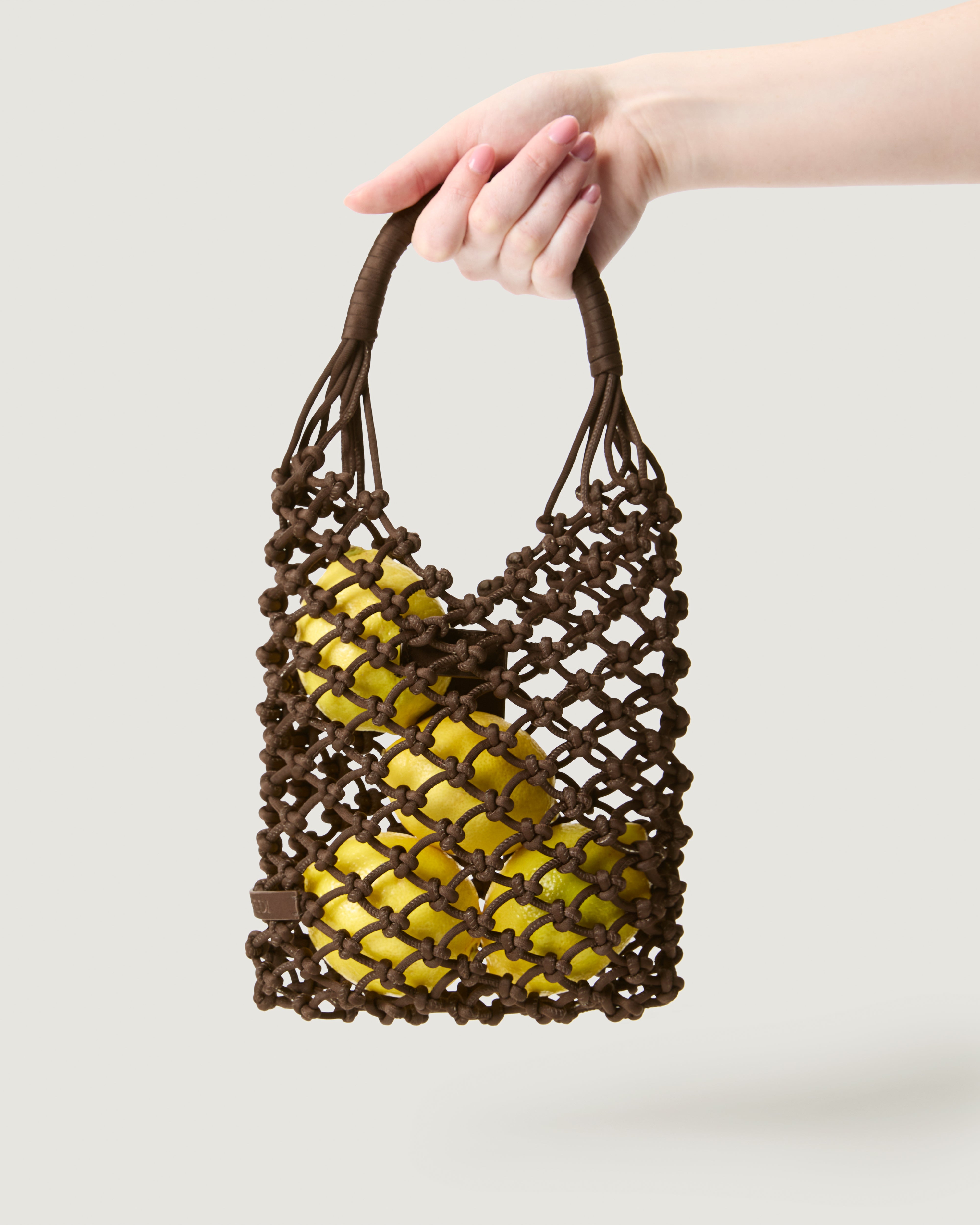 Hand holding small woven neoprene net bag in chocolate brown with fruit inside