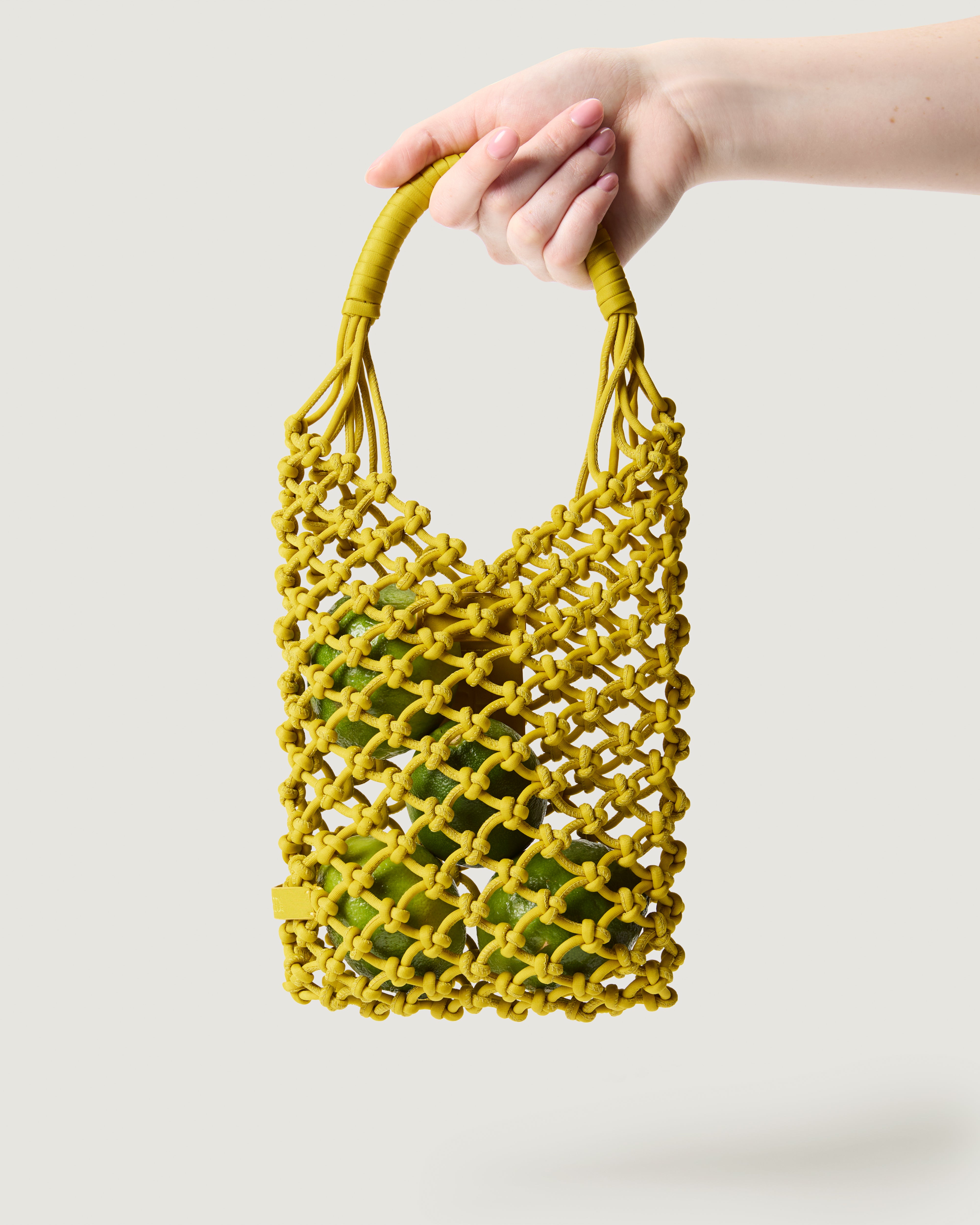 Arm holding small woven neoprene net bag in golden chartreuse with fruit inside