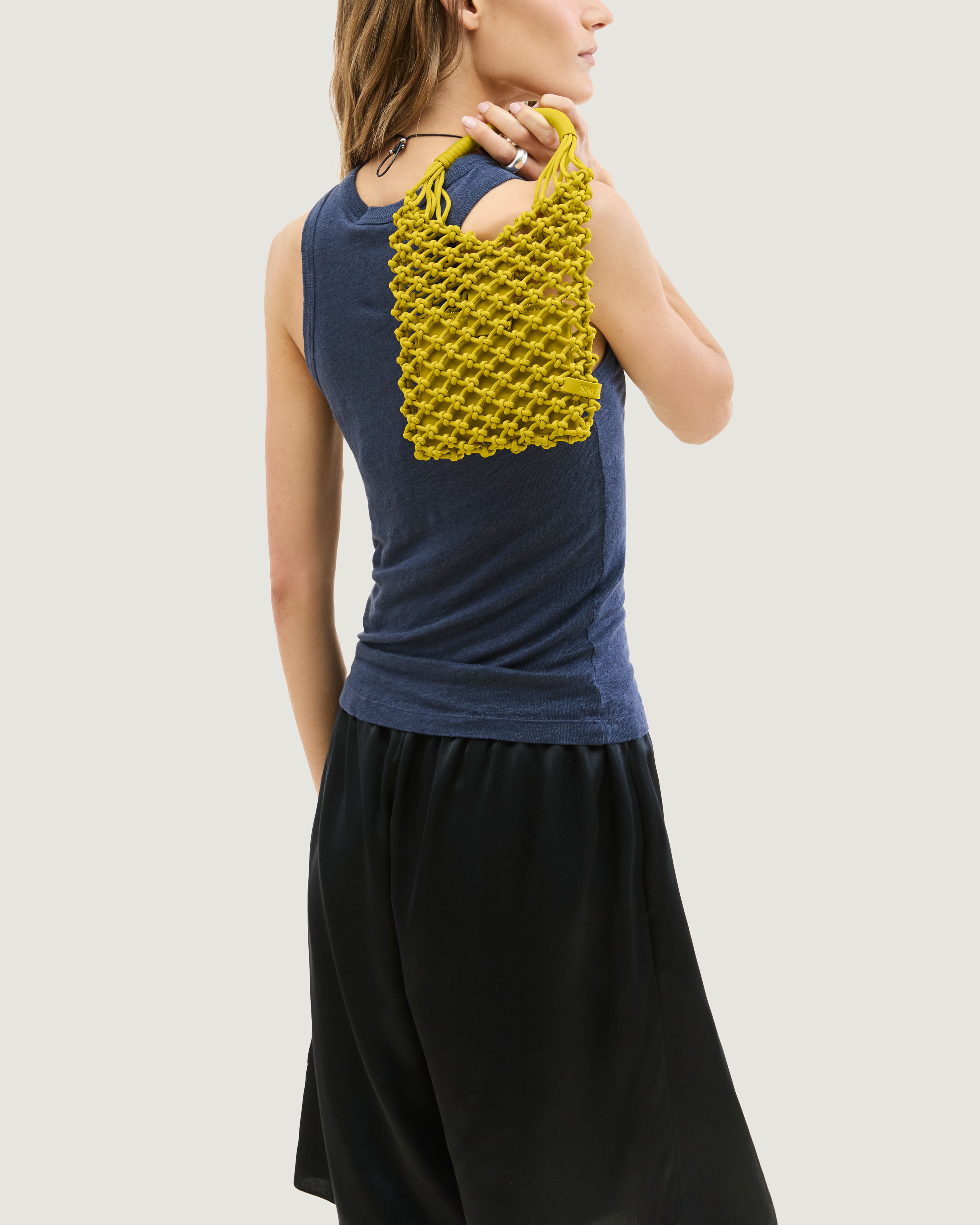 Model holding woven neoprene net bag in golden chartreuse over her shoulder