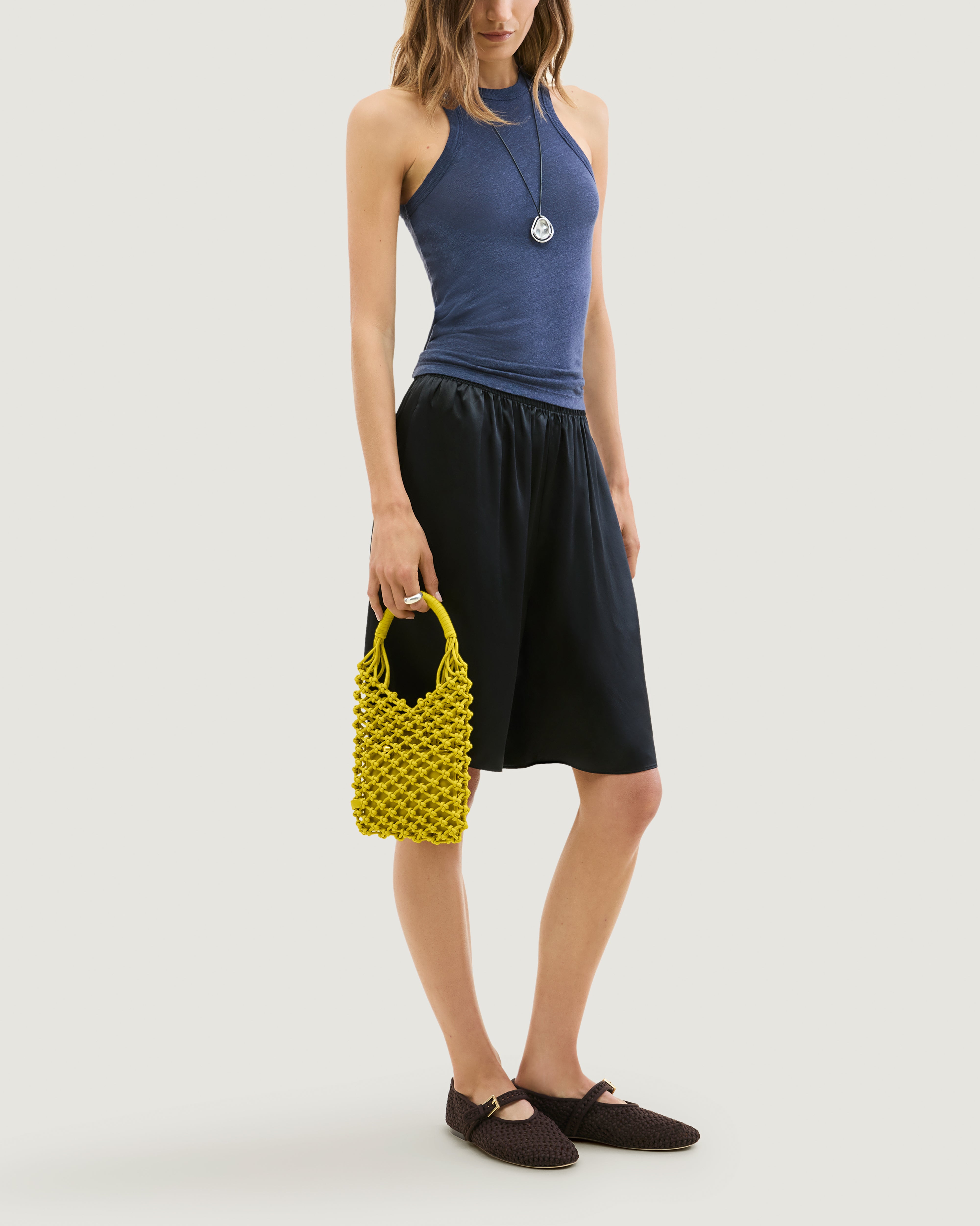 Model holding woven neoprene net bag in golden chartreuse at her side