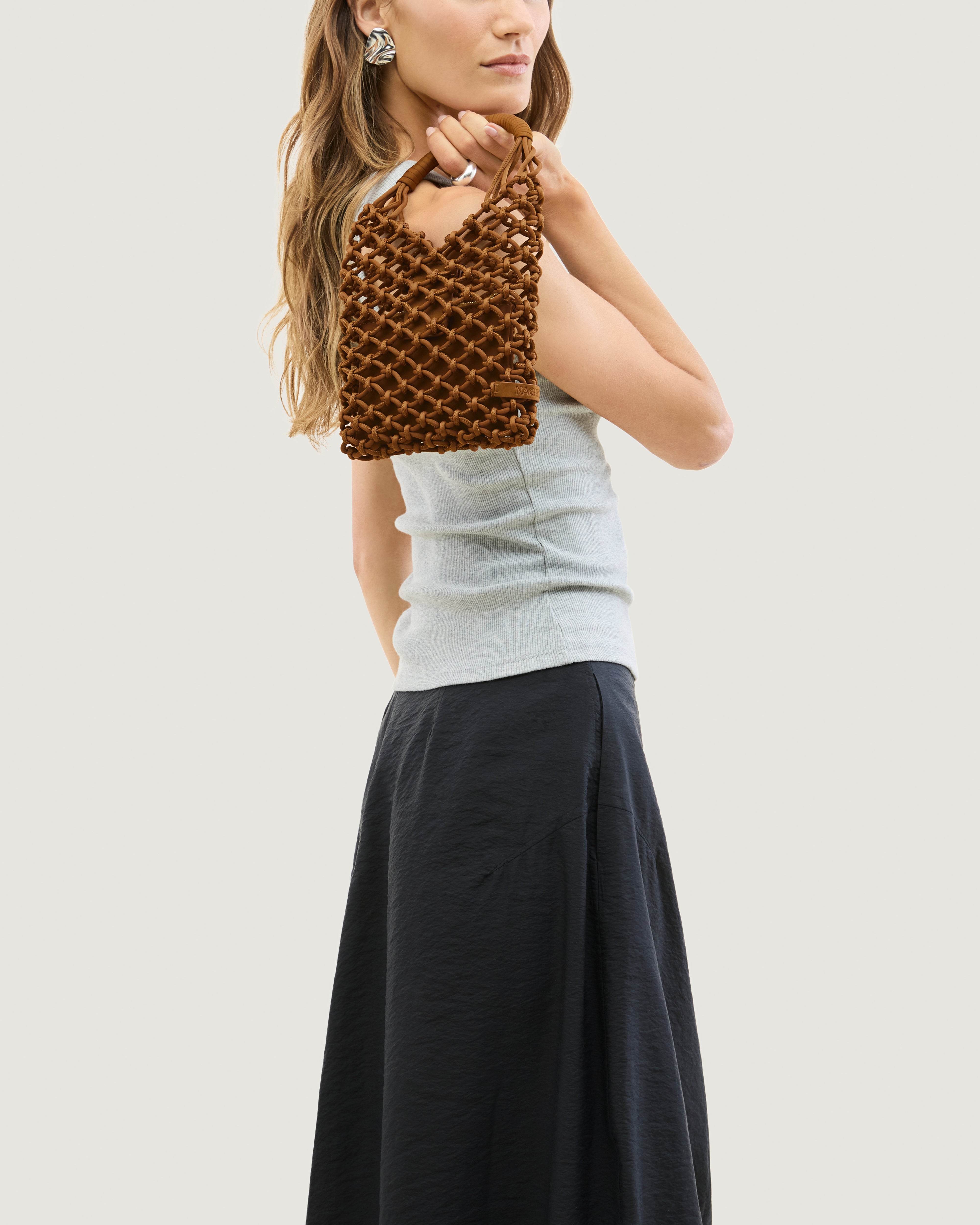 Model holding woven neoprene net bag in saddle brown over her shoulder