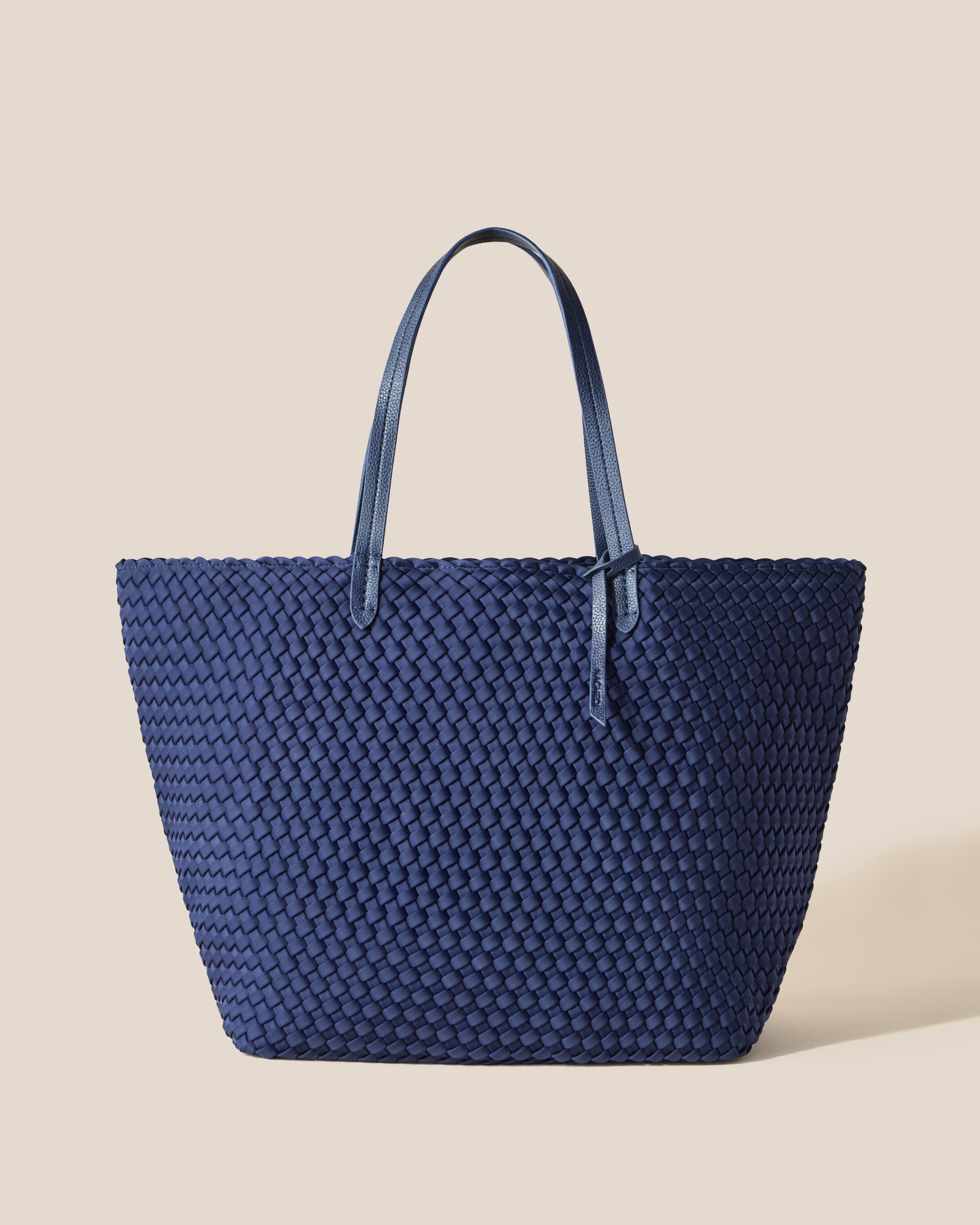 Jetsetter Tote in Ink Blue, a navy blue tone, in handwoven neoprene, featuring a top zip closure, and vegan leather handles.