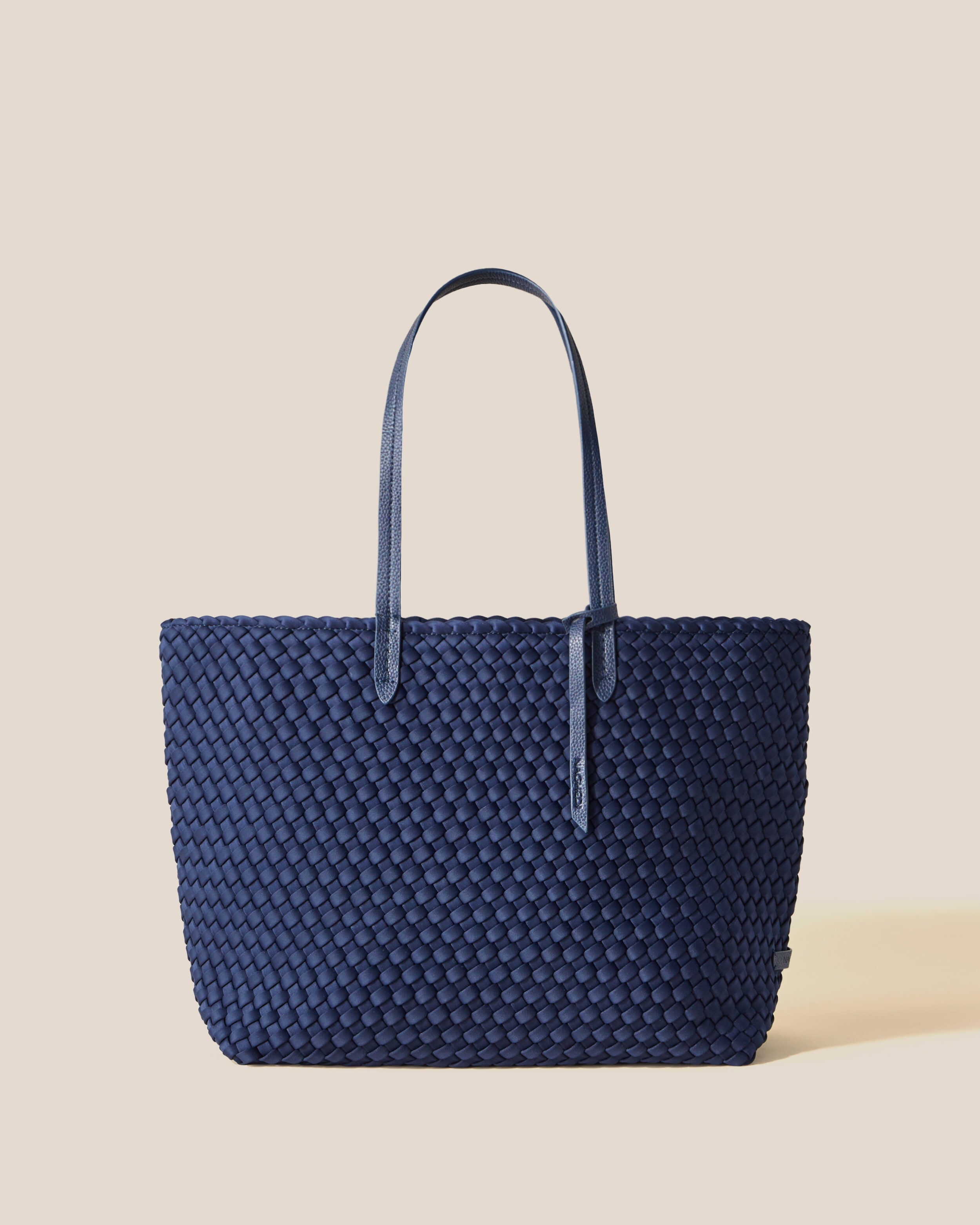 Jetsetter Tote in Ink Blue, a navy blue tone, in handwoven neoprene, featuring a top zip closure, and vegan leather handles.