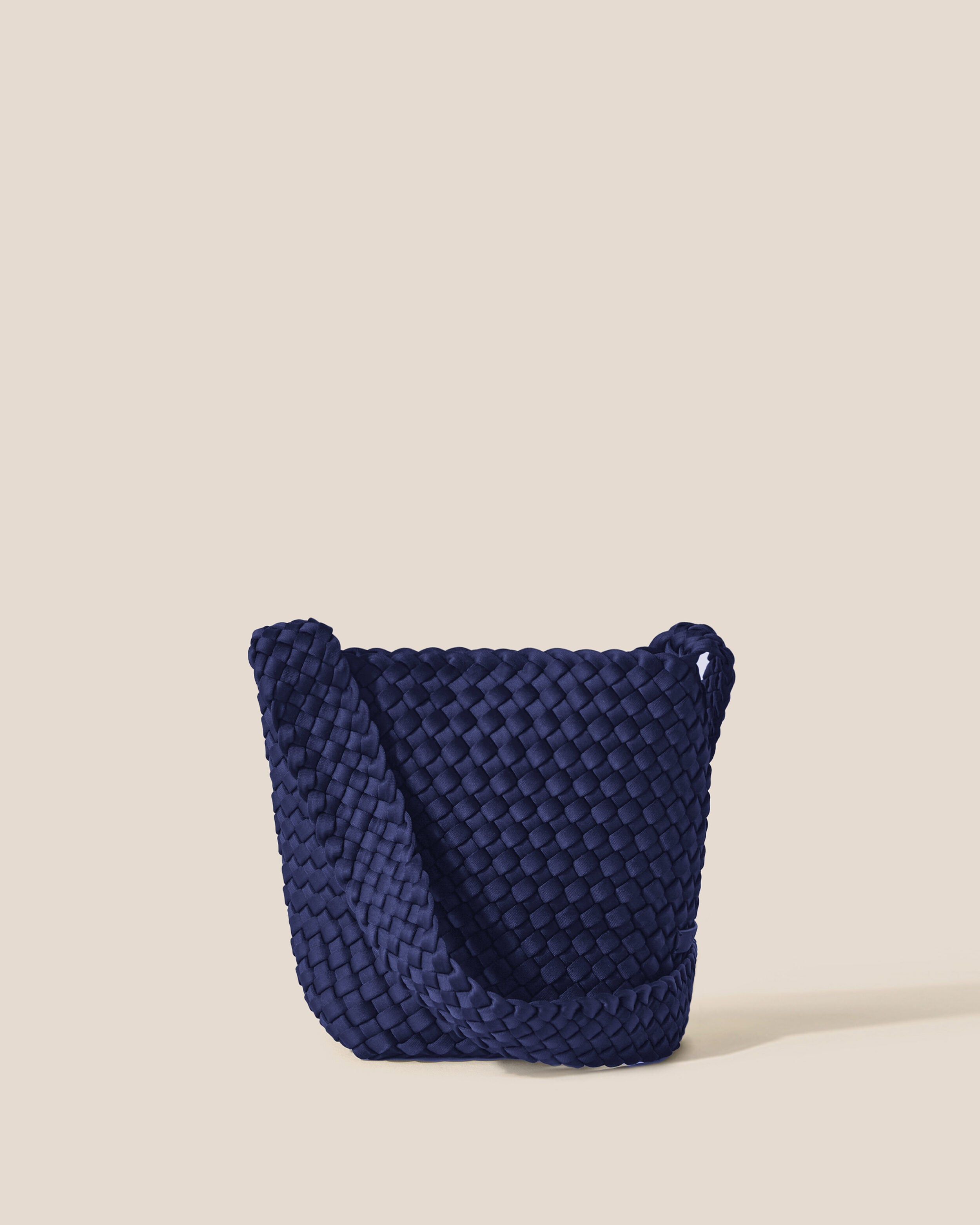 Laguna Crossbody in Ink Blue, a navy blue tone, in handwoven neoprene, featuring an open top with magnetic snap closure, and handwoven crossbody strap lays comfortably flat.